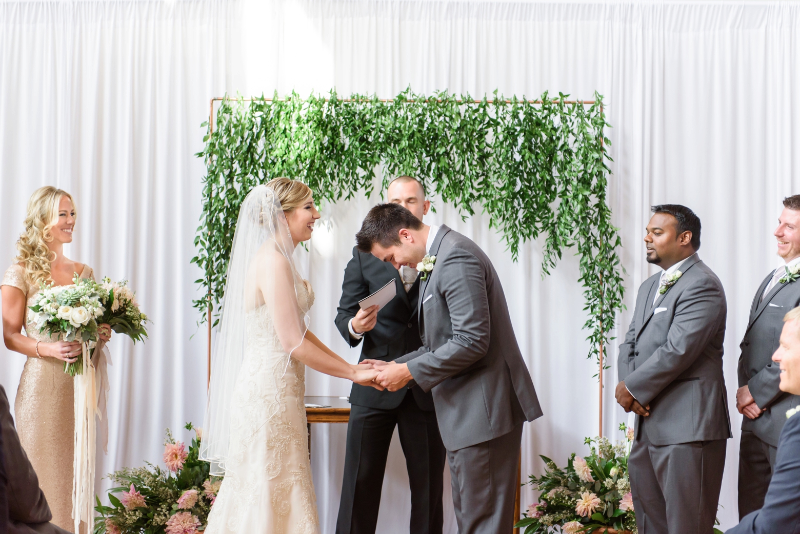 Groom laughs during the ceremony under a greenery arch