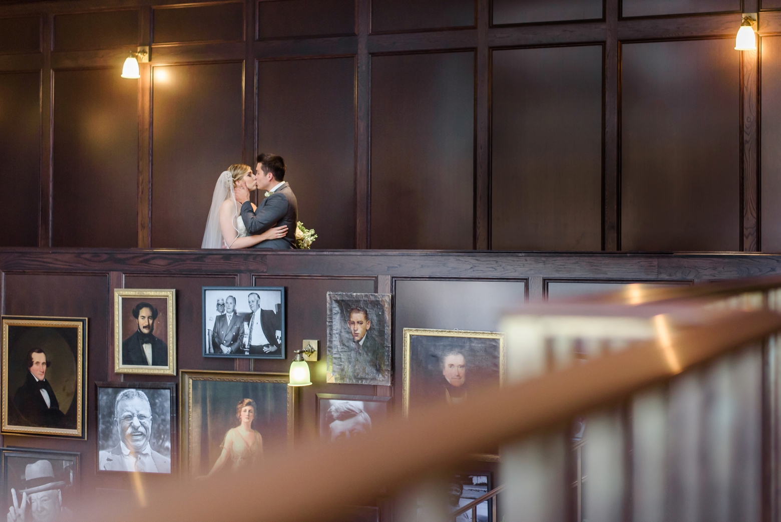 Bride and Groom kiss above the portrait wall inside the Oxford Exchange