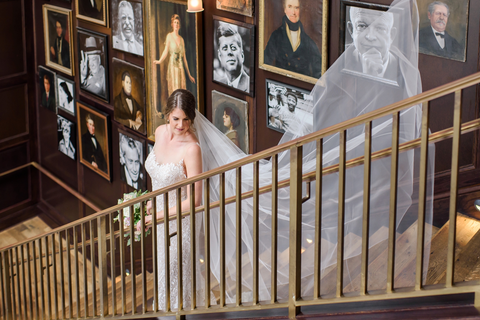 A bride stands on the grand staircase of Oxford Exchange while her cathedral veil blows