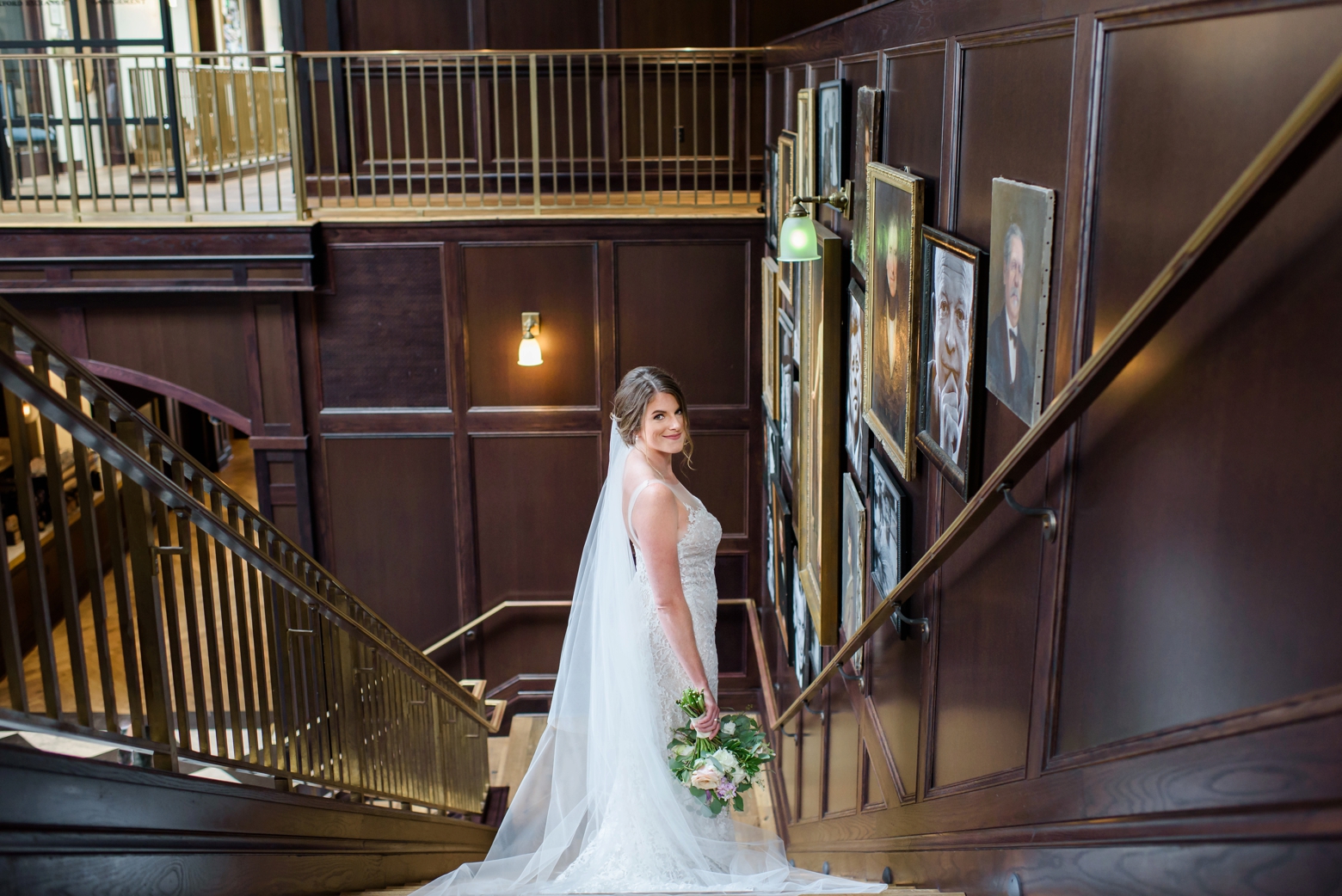 A bride wears a cathedral veil and strapped wedding gown while standing on a staircase