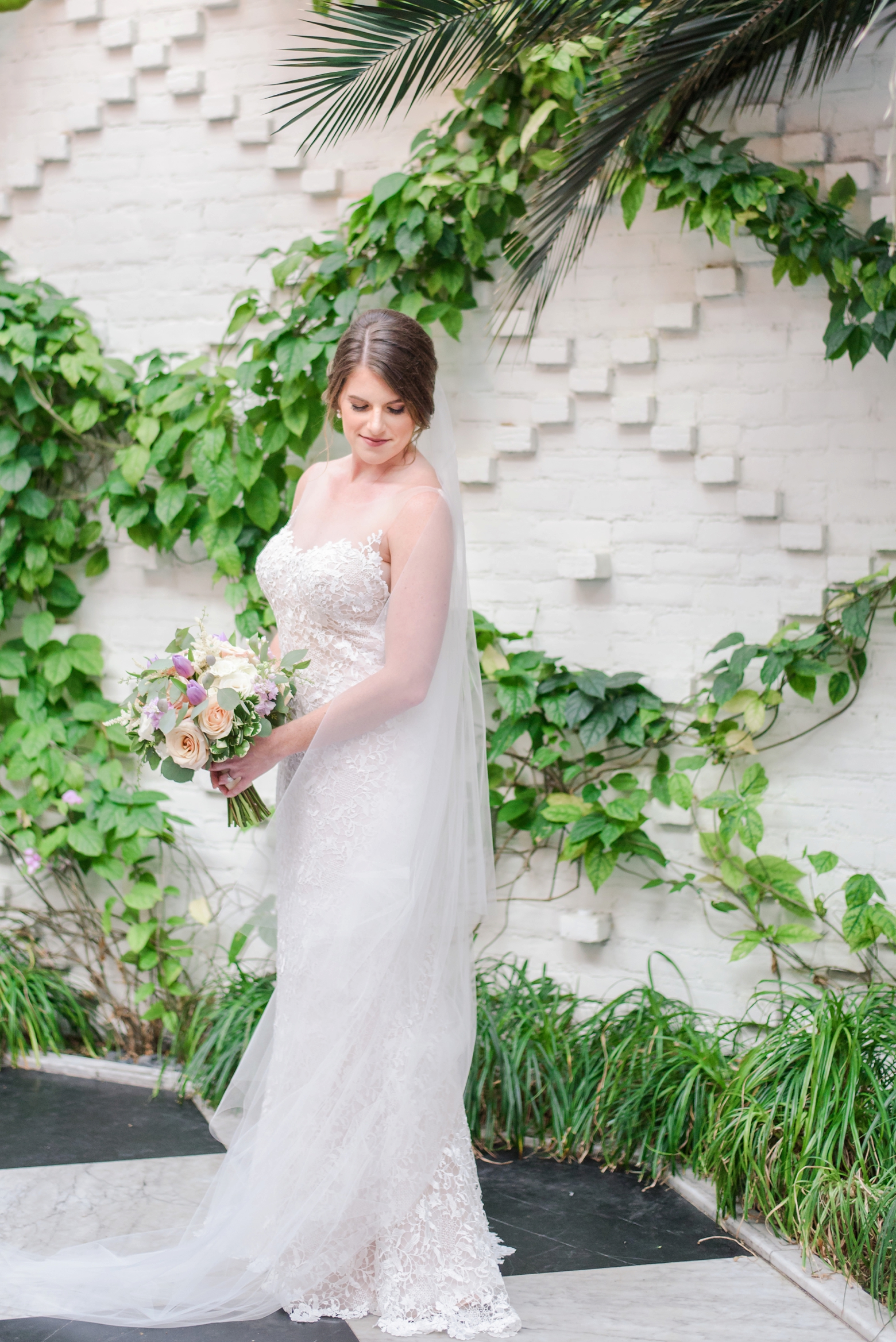 Bride standing in front of a white brick wall and greenery during her bridal session
