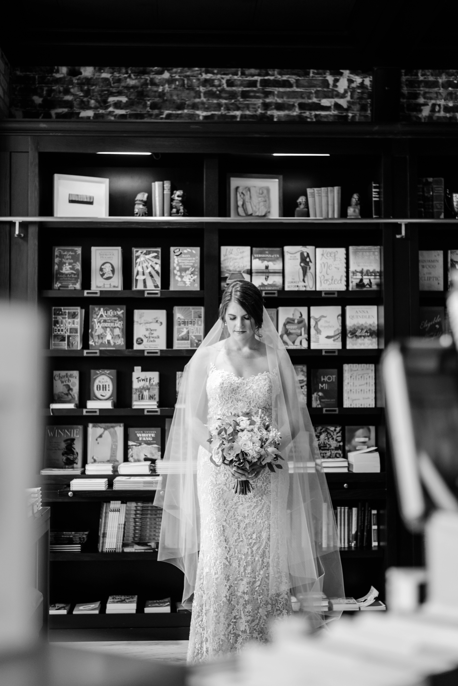 Bride stands looking at her flowers in the library of Oxford Exchange