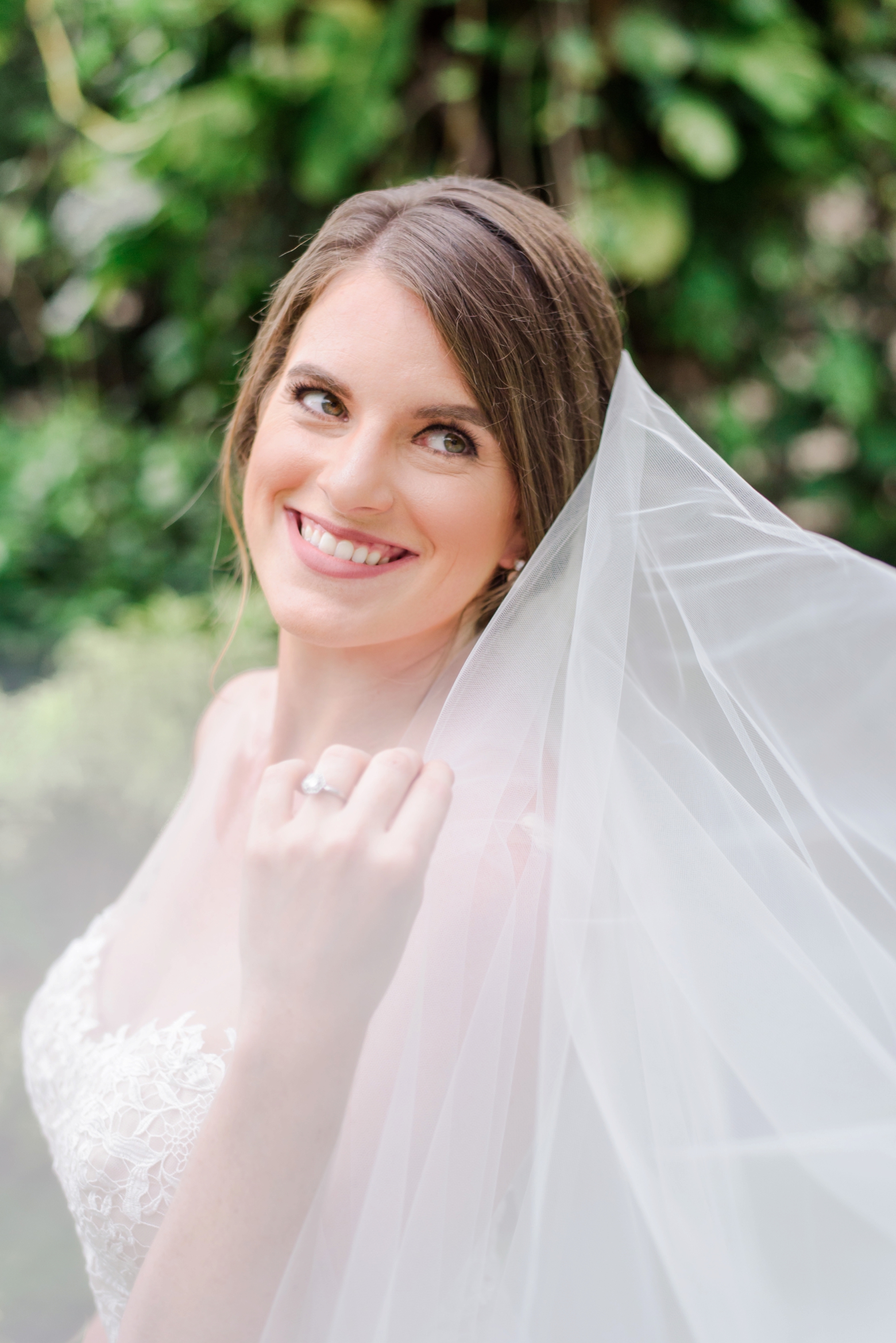 Bride shows off her engagement ring while holding her veil