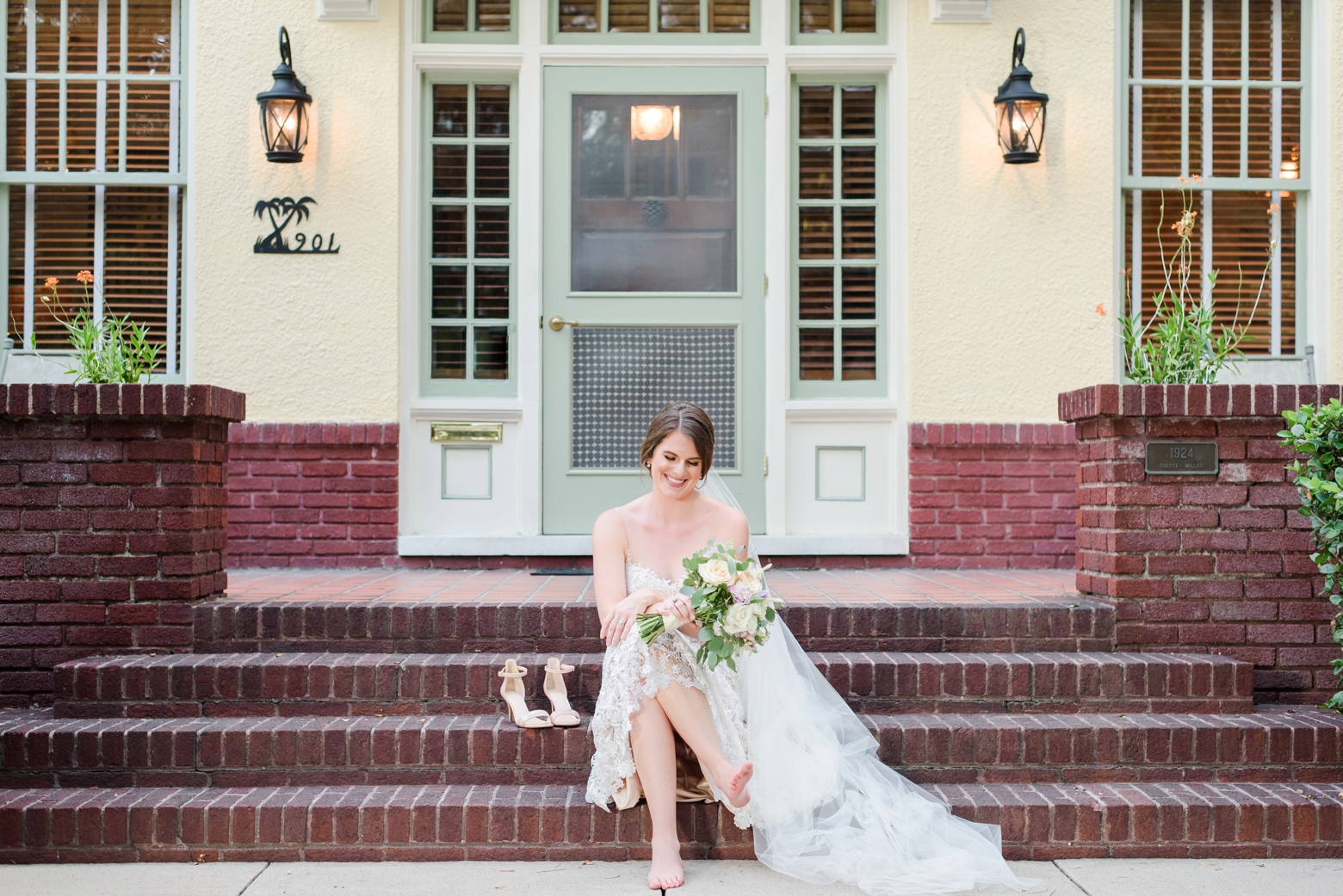Bride sits next to her shoes and laughs on the staircase of her childhood home