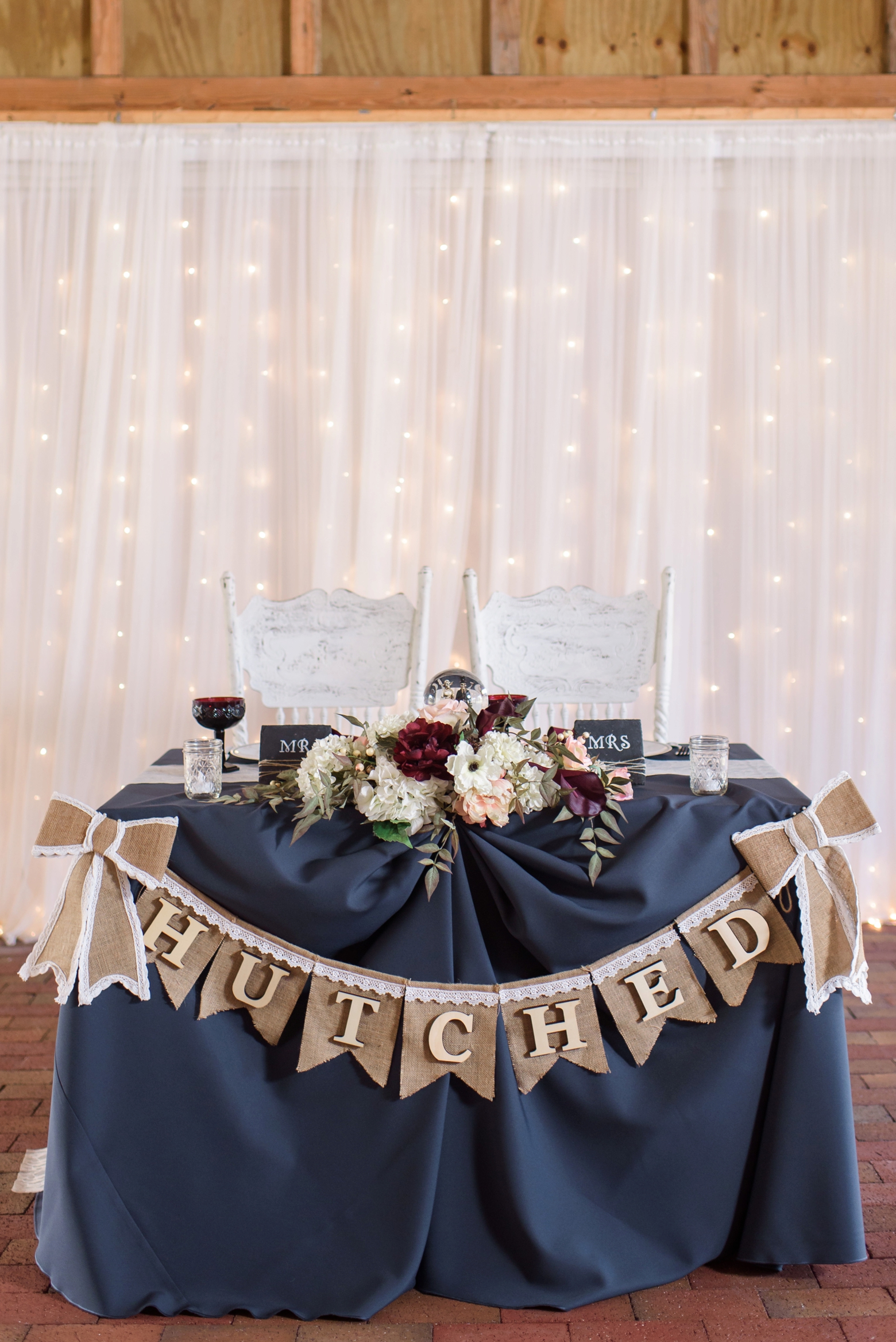The head table decorated with a banner and large floral arrangement in front of twinkle lights