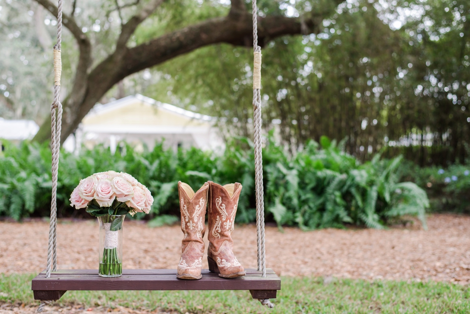 Brides cowboy boots and rose filled bouquet on a tree swing before a cross creek wedding ceremony