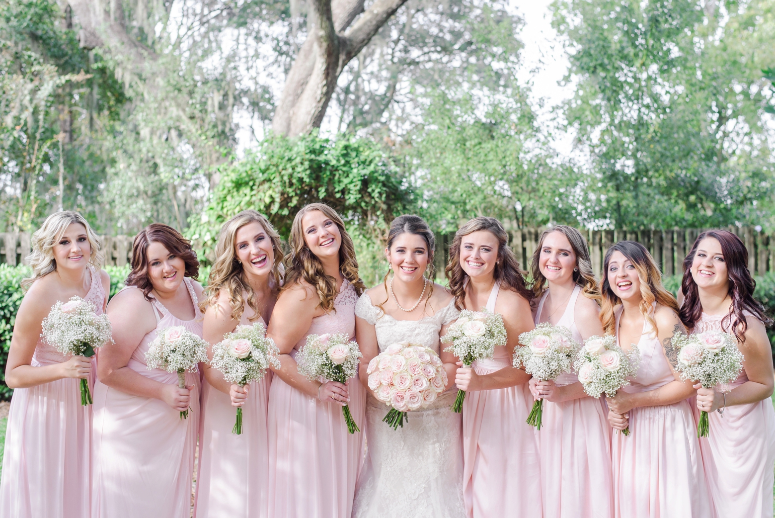 Bride and her Bridesmaids holding their florals stand in a line and smile for a formal portrait