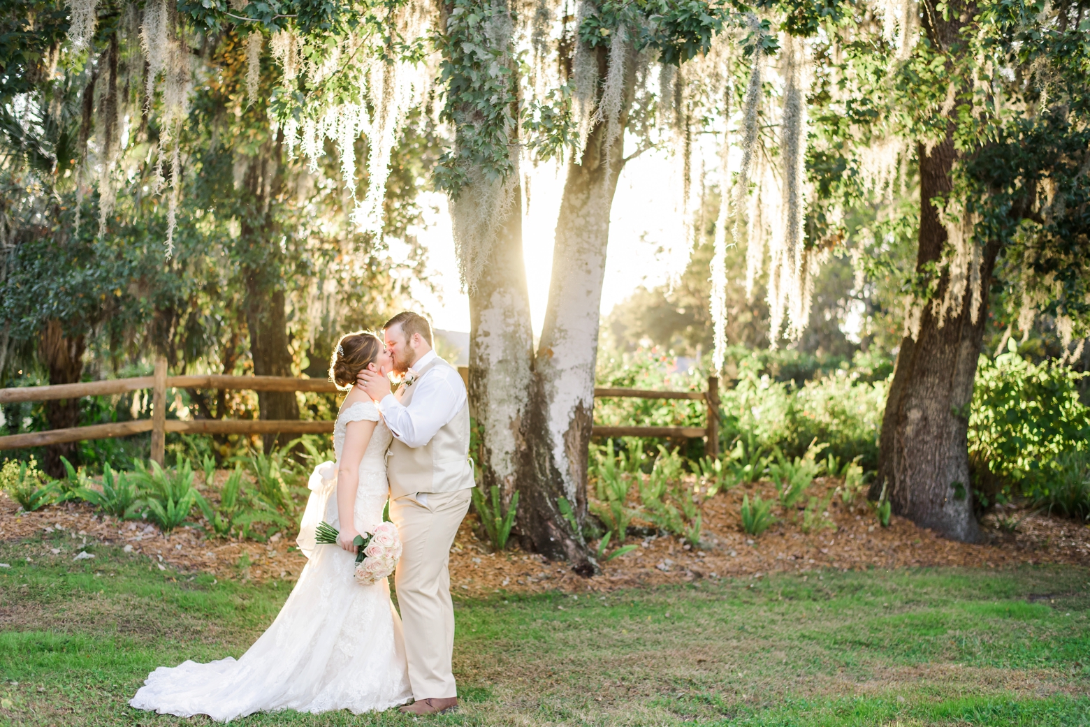 Bride and Groom kiss while the sun sets behind them through the spanish moss after their cross creek wedding ceremony