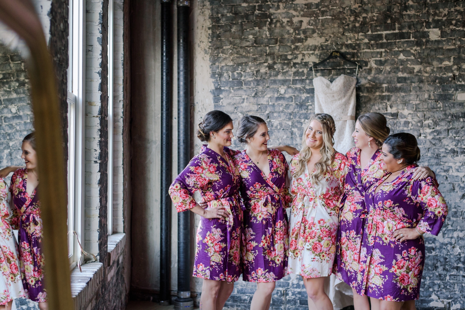 Bride and her Bridesmaids in their silk robes pose in a brick room at the Oxford Exchange in Tampa, FL