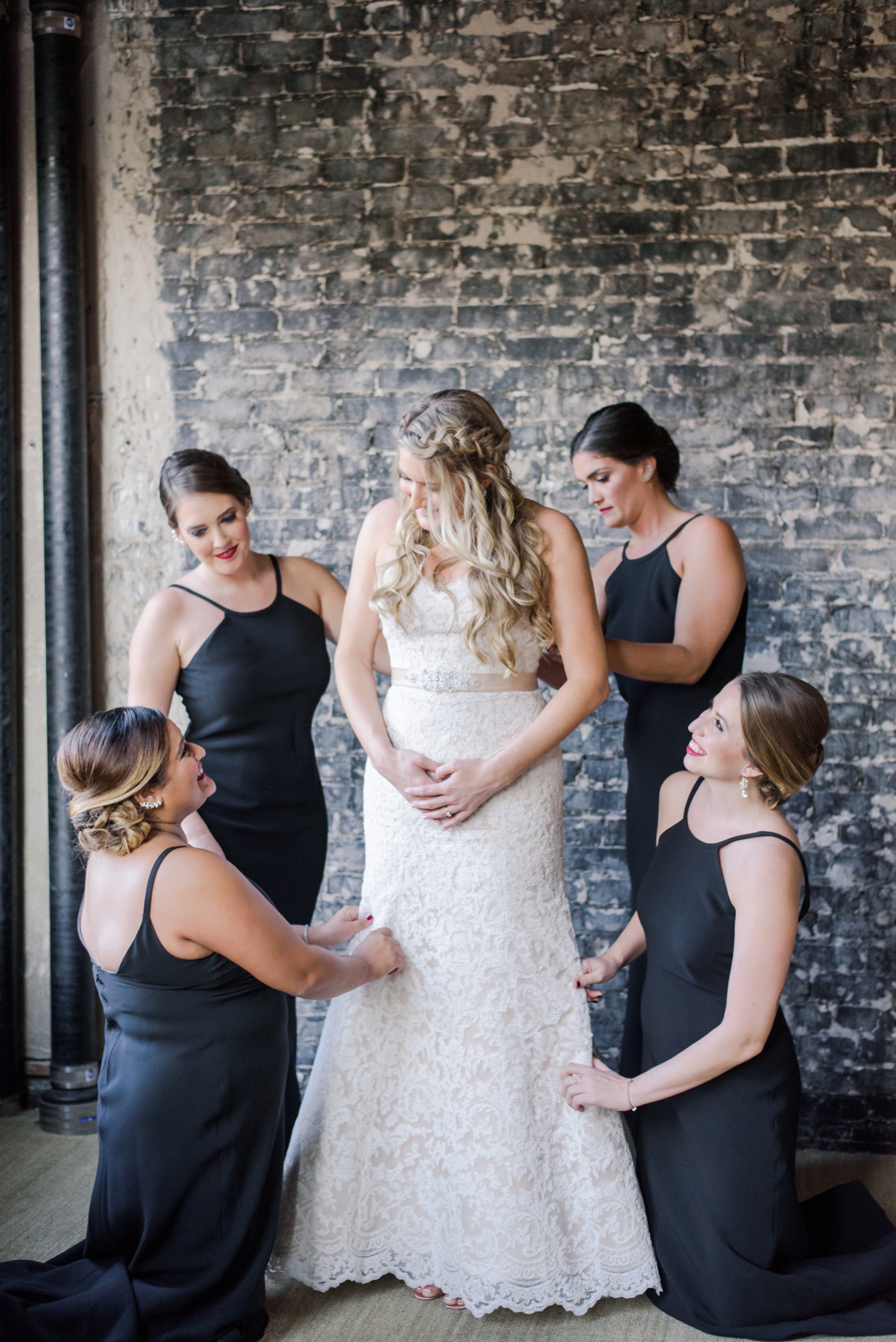 The Bride surrounded by her Bridesmaids as they assist in adjusting the dress to absolute perfection