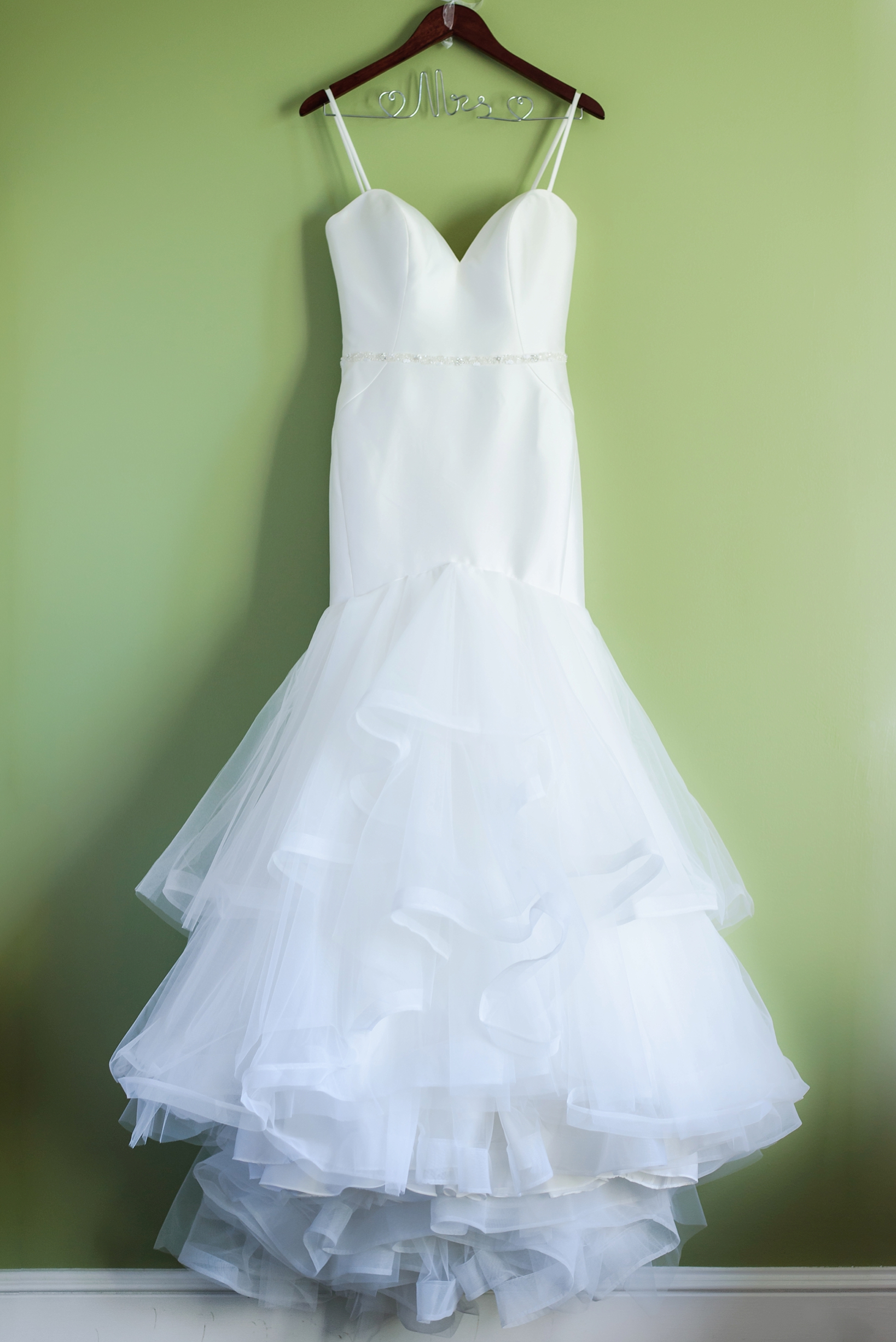 Bridal gown with tule details against a green wall photographed by Sarah & Ben Photography