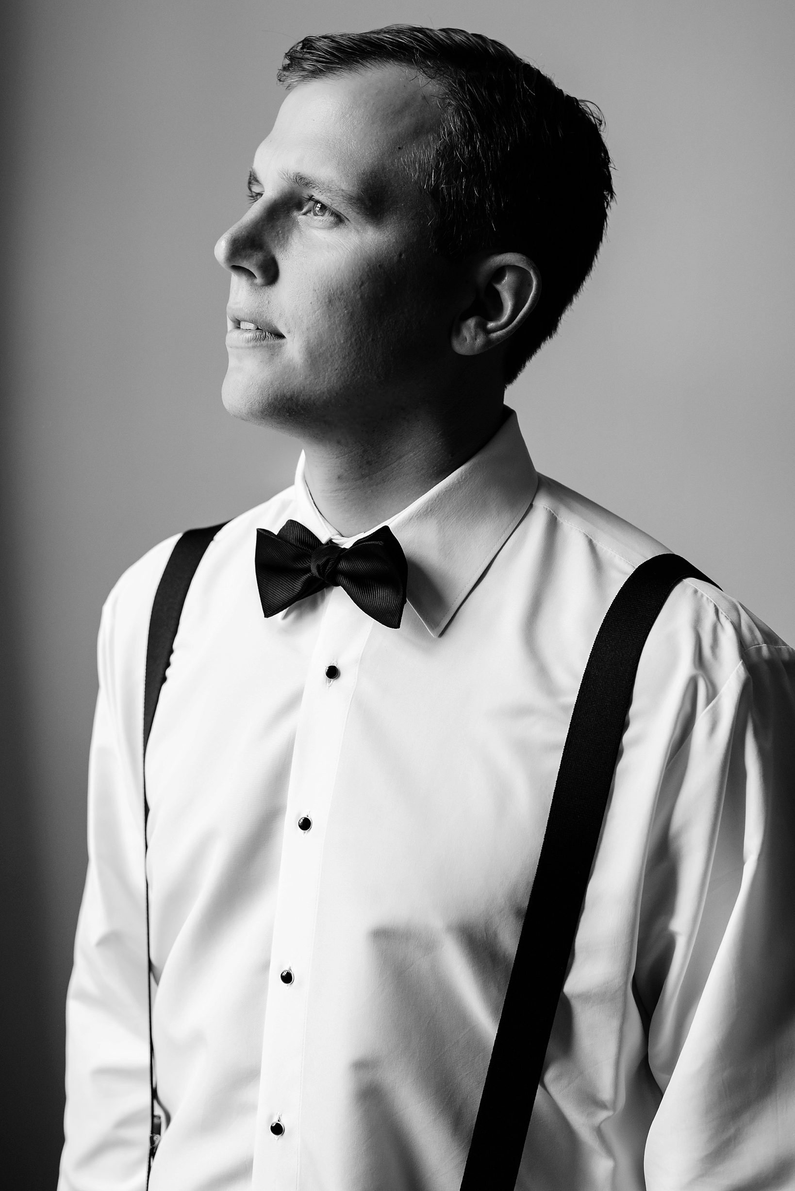 Black and white image of the groom in his shirt and suspenders.