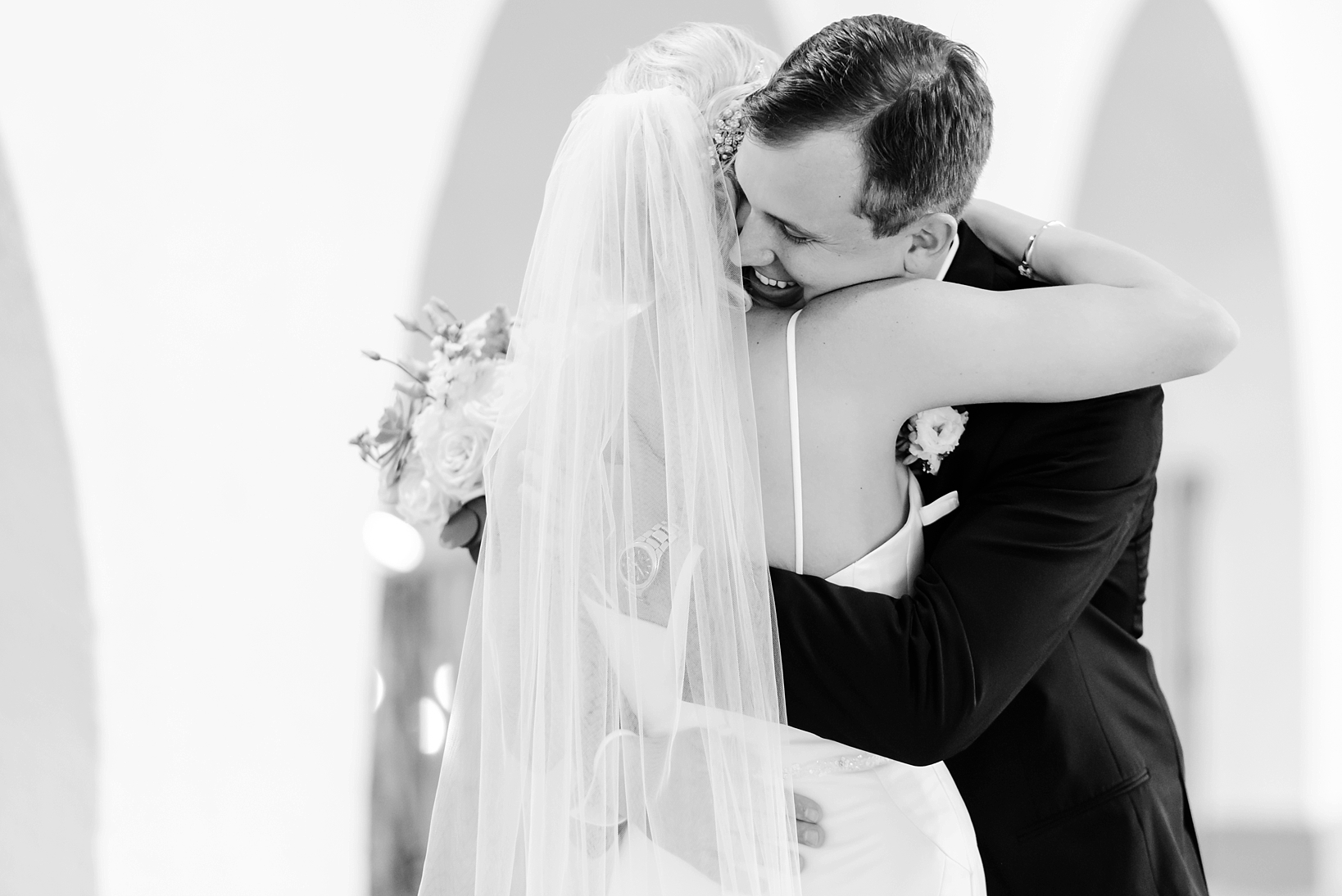 Black and white image of a groom hugging his bride during their first look