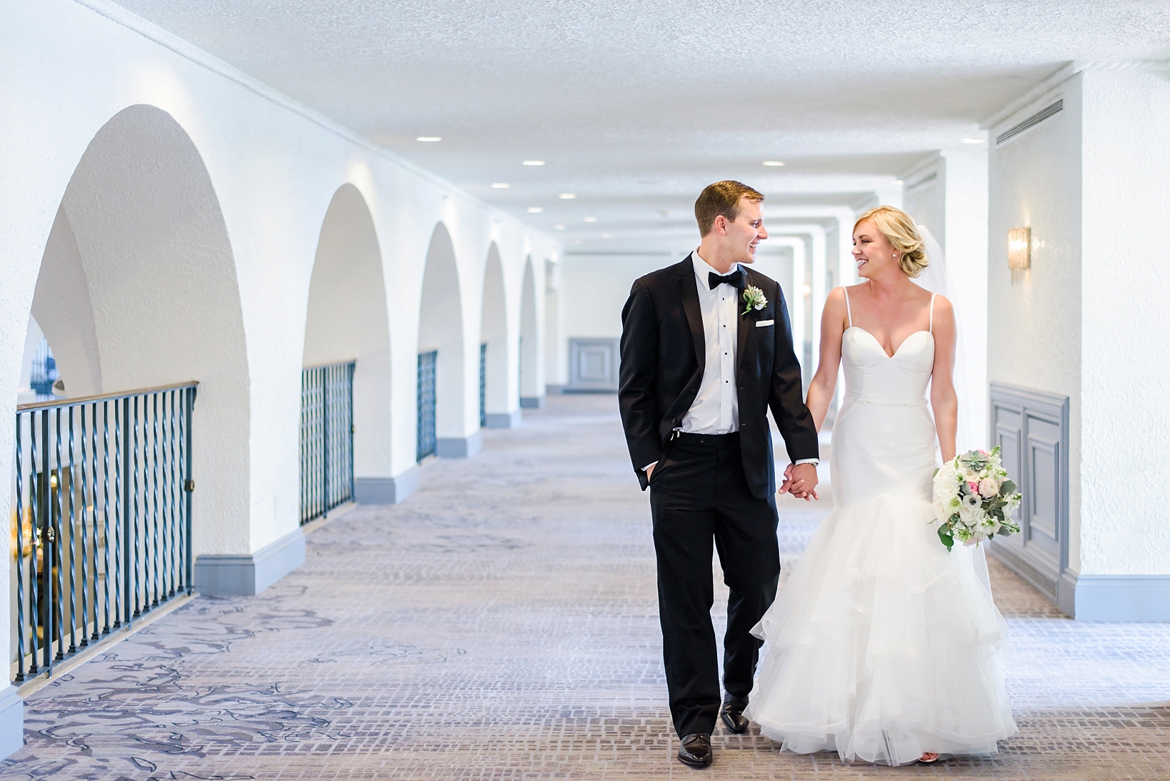 Bride and groom holding hands as they walk down the hallways of a hotel.