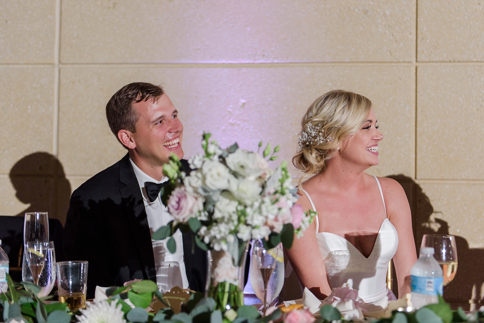During speeches, the newlyweds laugh at the stories being told.