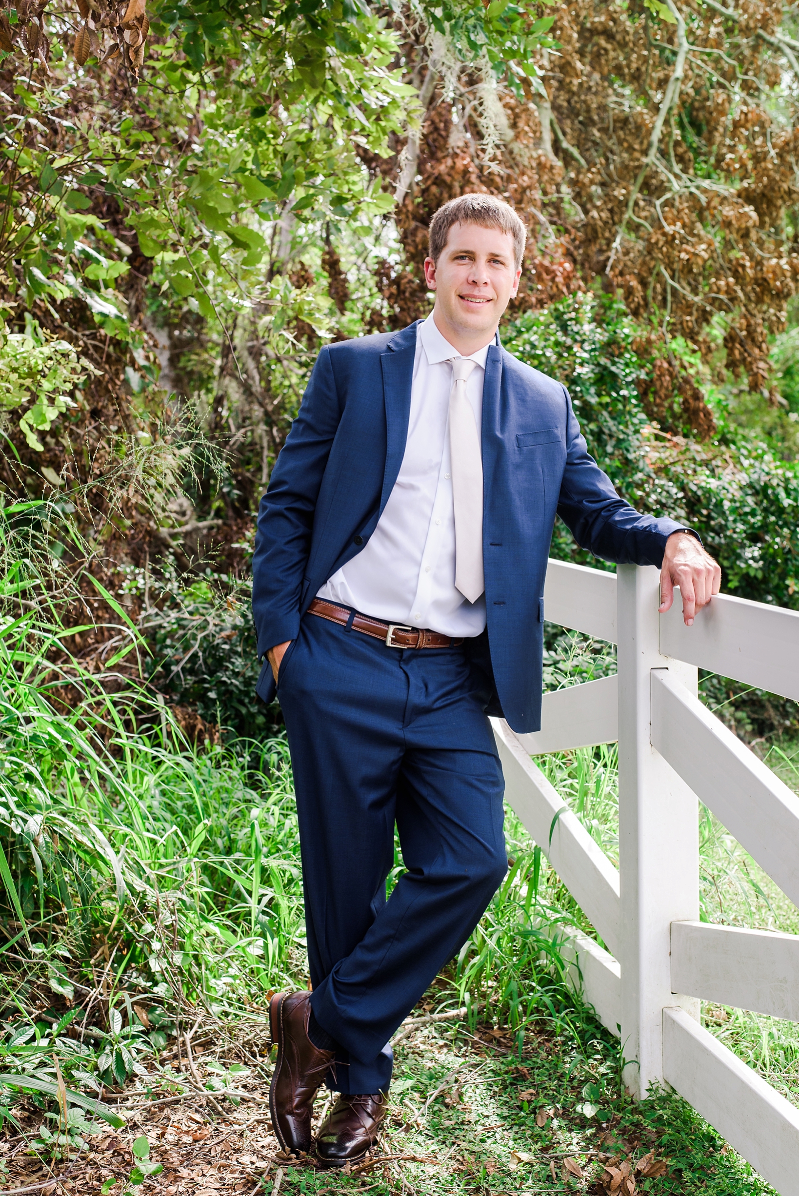 Groom leaning on a white fence