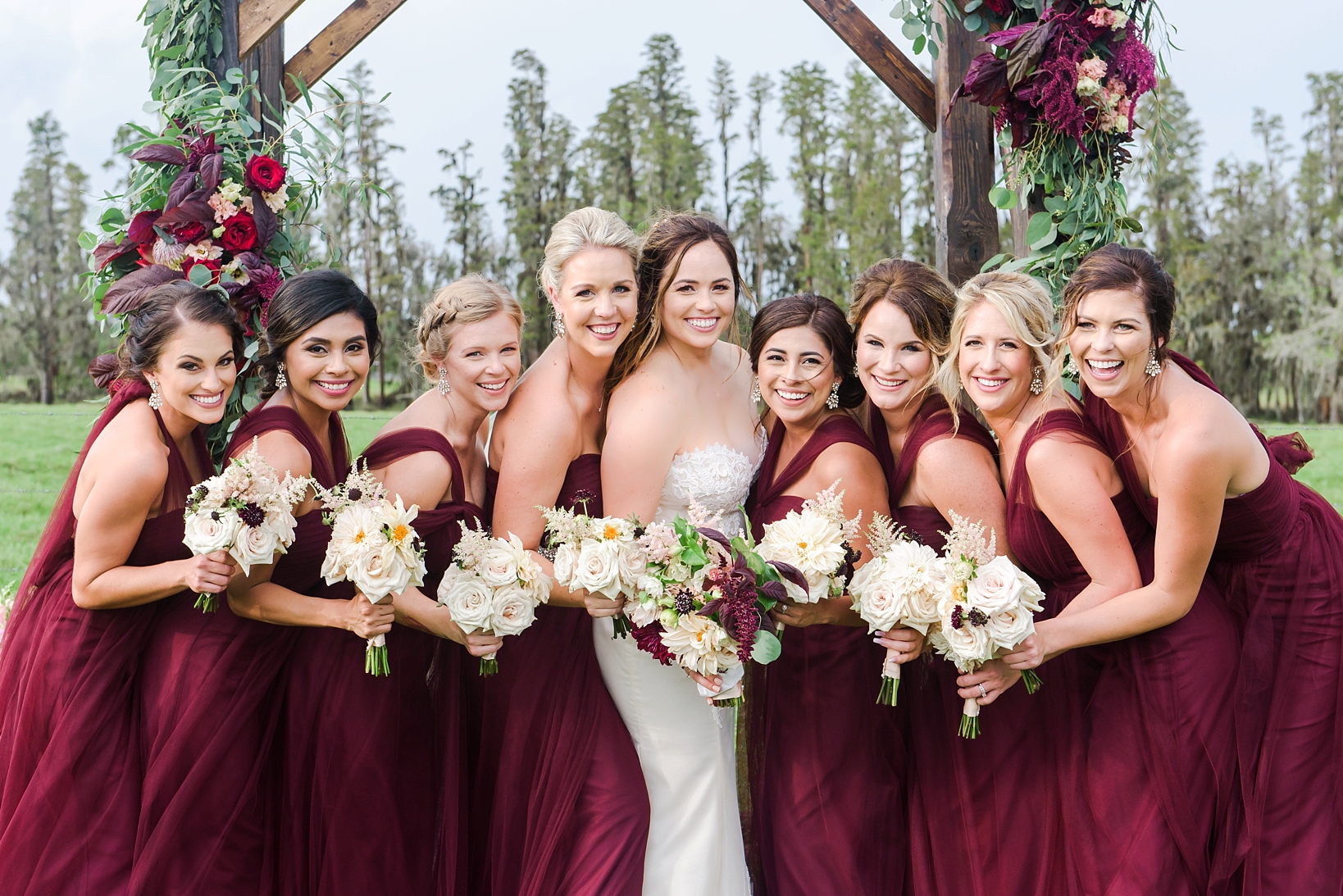 Bride and her bridesmaids at the wedding arch holding floral bouquets