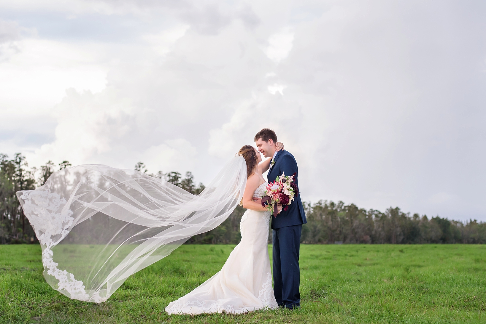 Bride and her groom embrace as the wind blows her cathedral veil