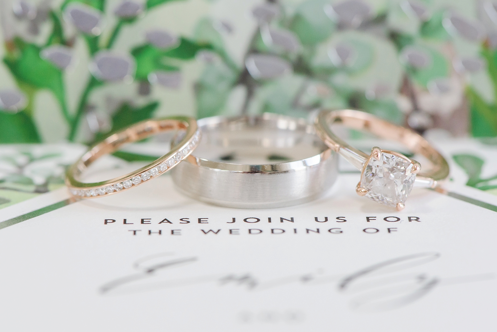 Wedding bands against a green and silver foil invitation