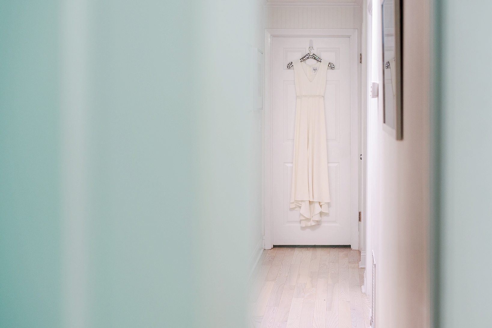The wedding dress hanging near a turquoise wall 
