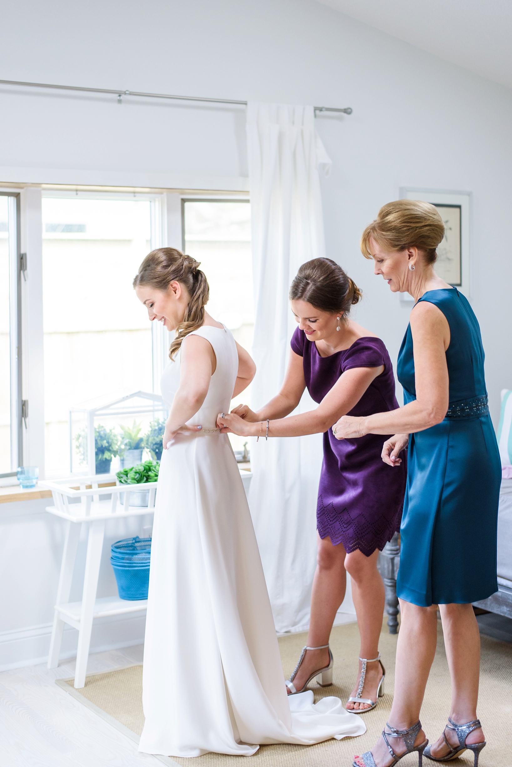 Bride getting into her dress with the help of her sister and mom