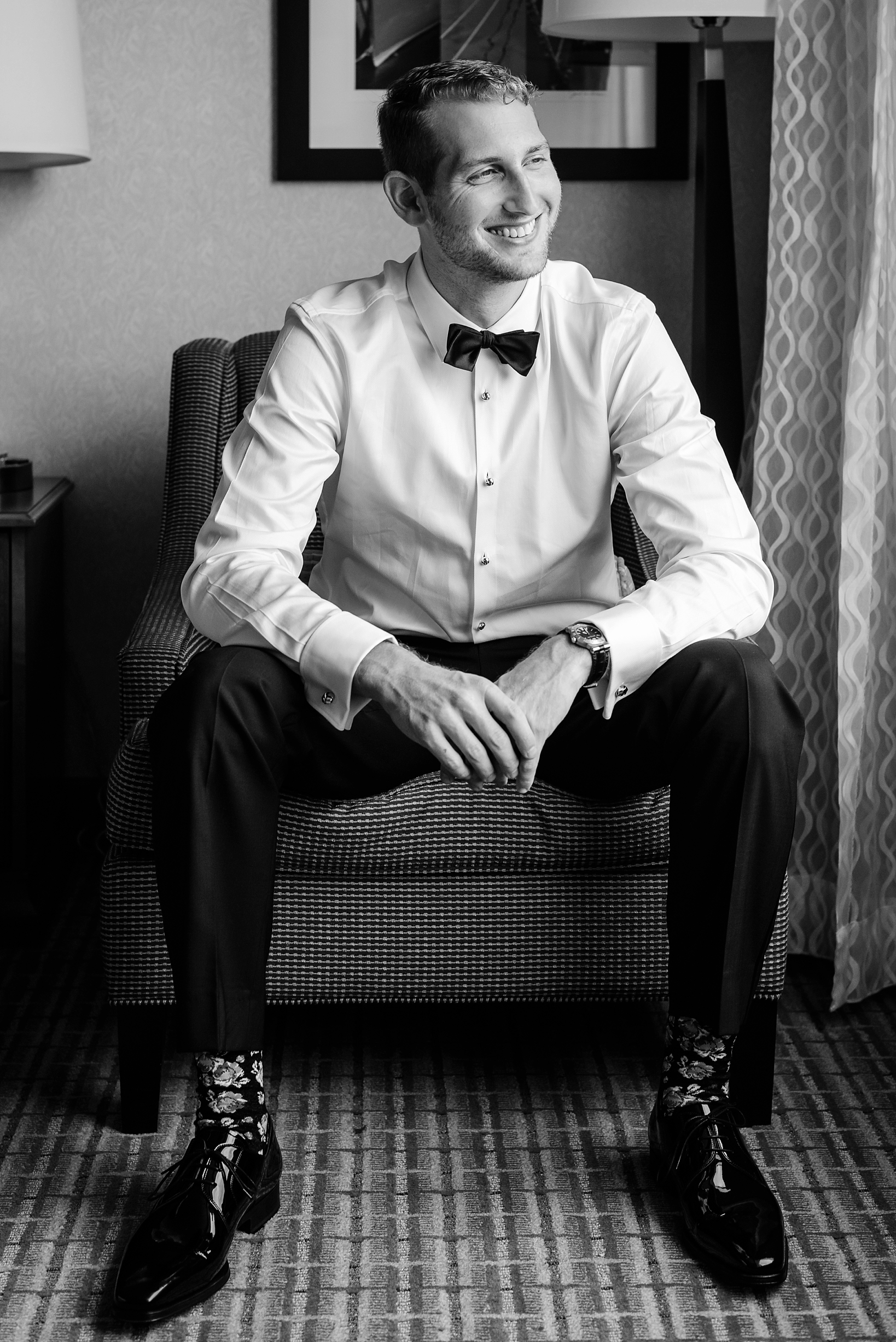 Black and white photo of an excited groom on his wedding day looking out a window