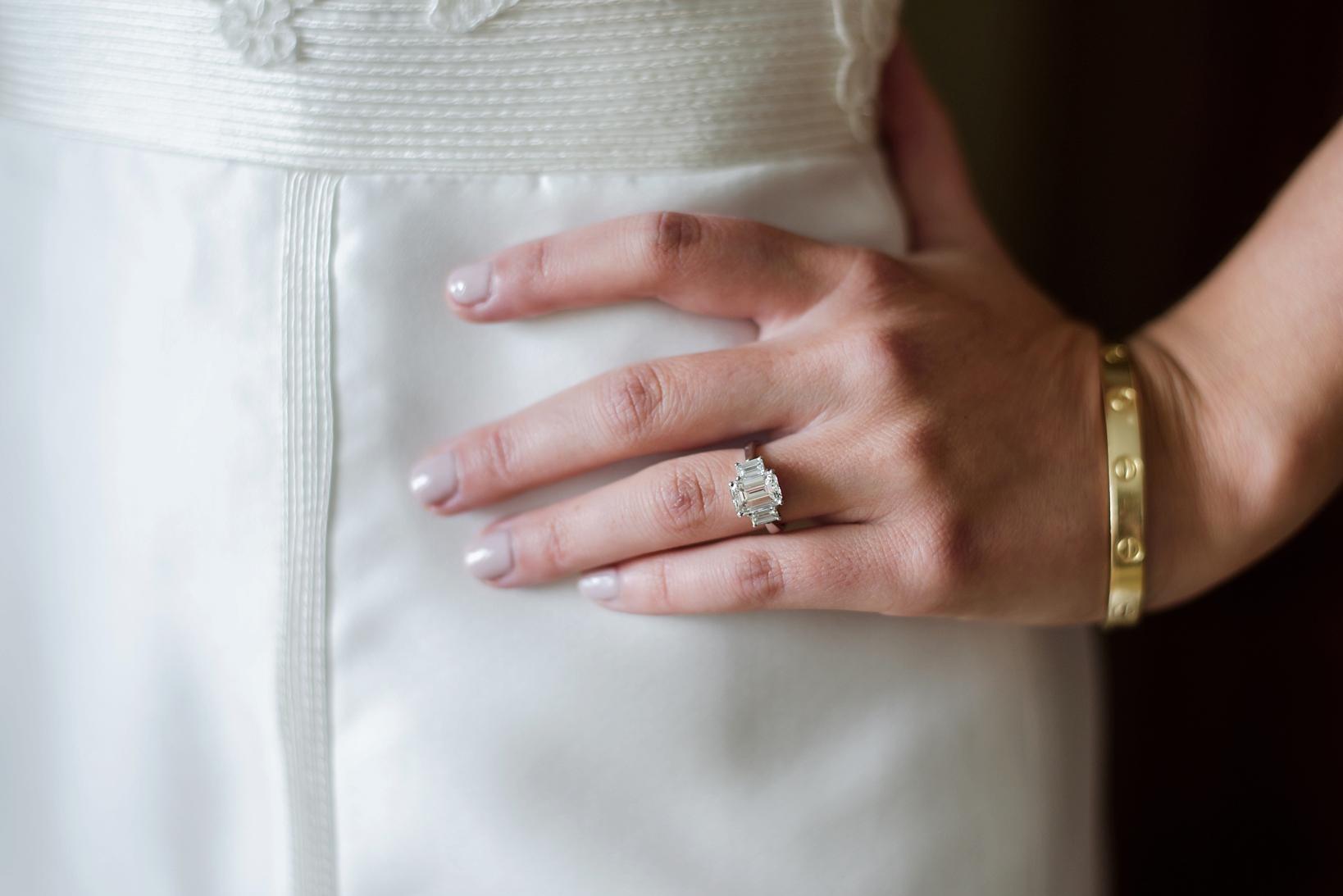 The bride's hand with engagement ring against her silk wedding dress