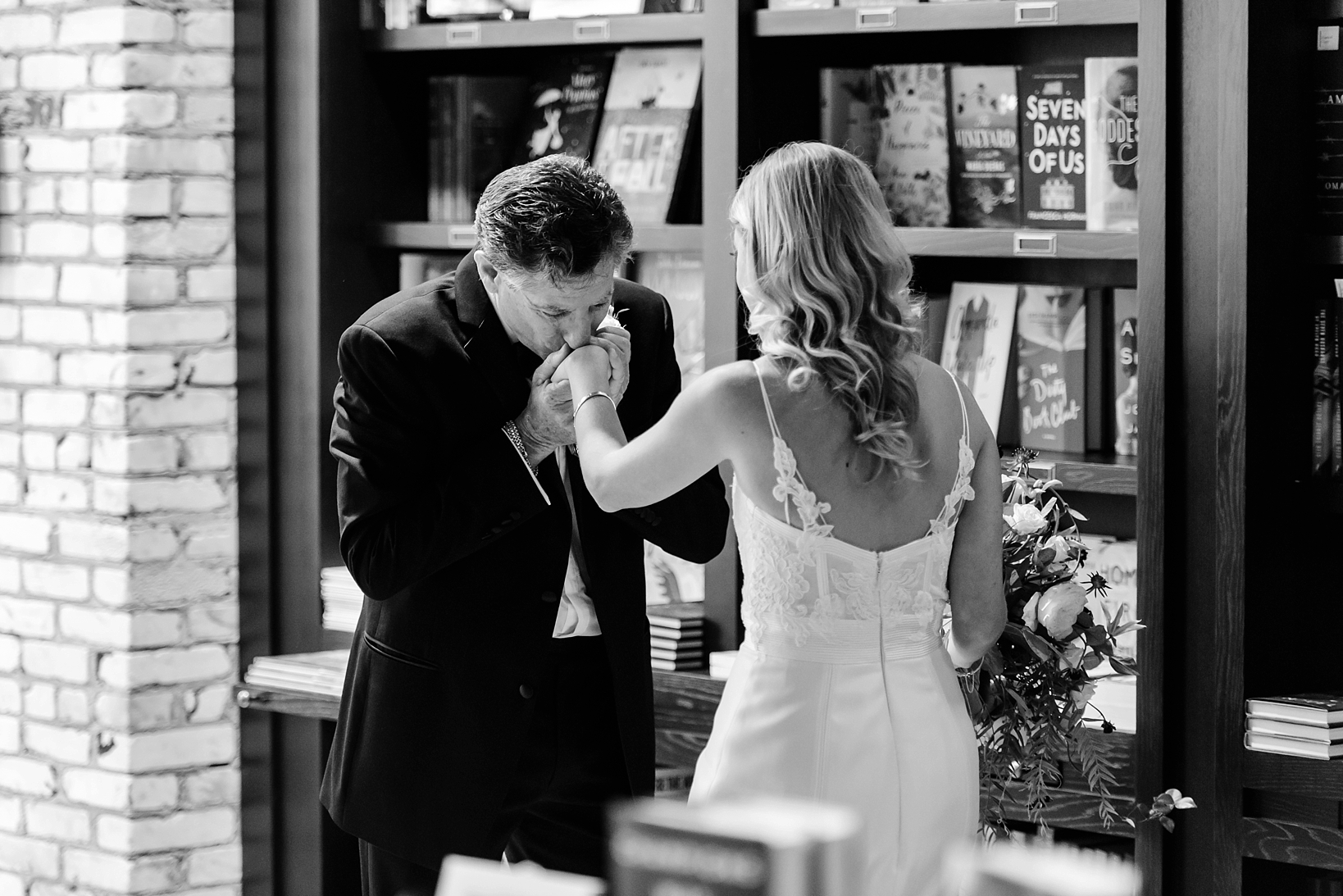 Father kisses his daughters hand in a bookstore after seeing her for the first time in her wedding dress