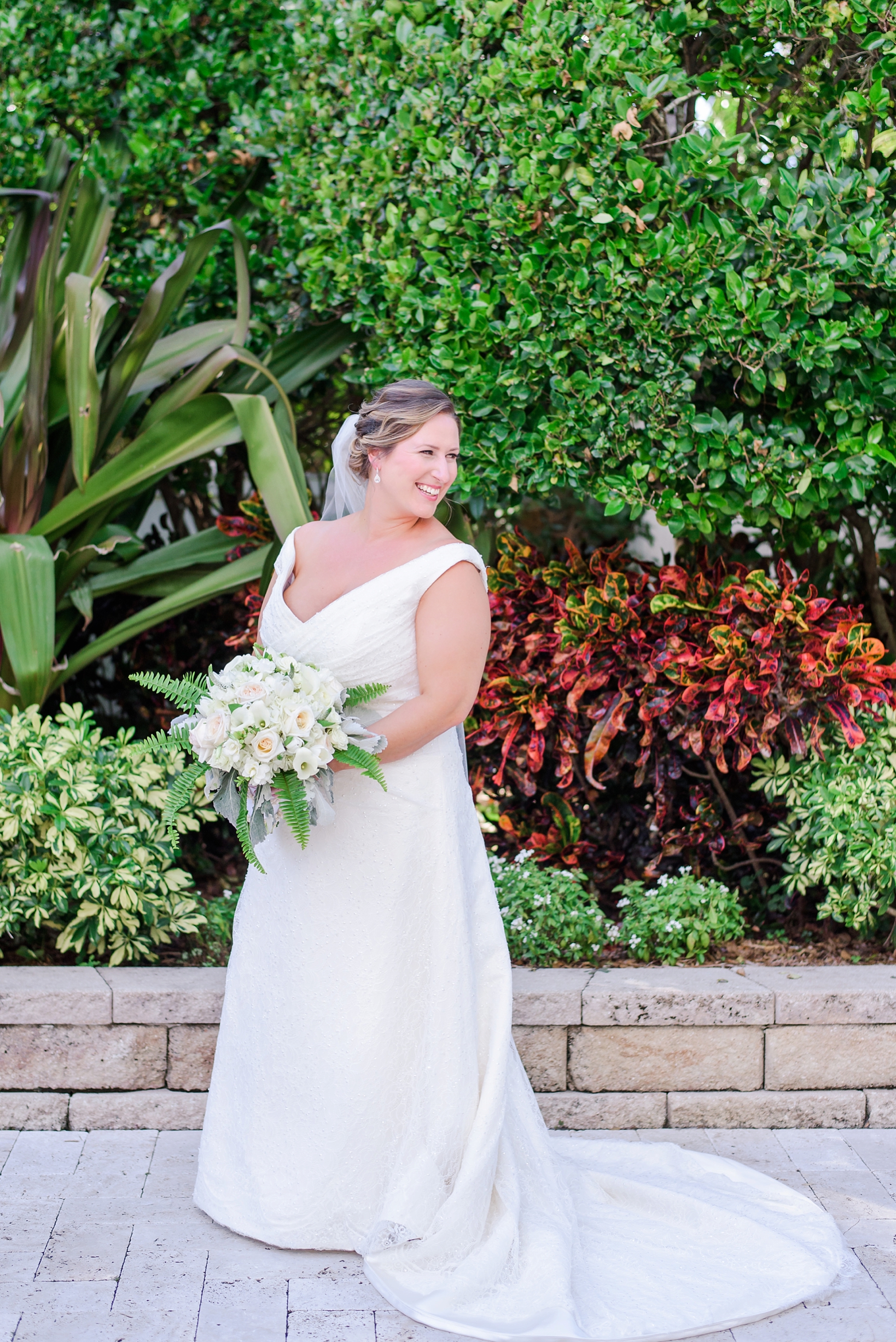 The bride holding her flower bouquet in front of some shrubberies 