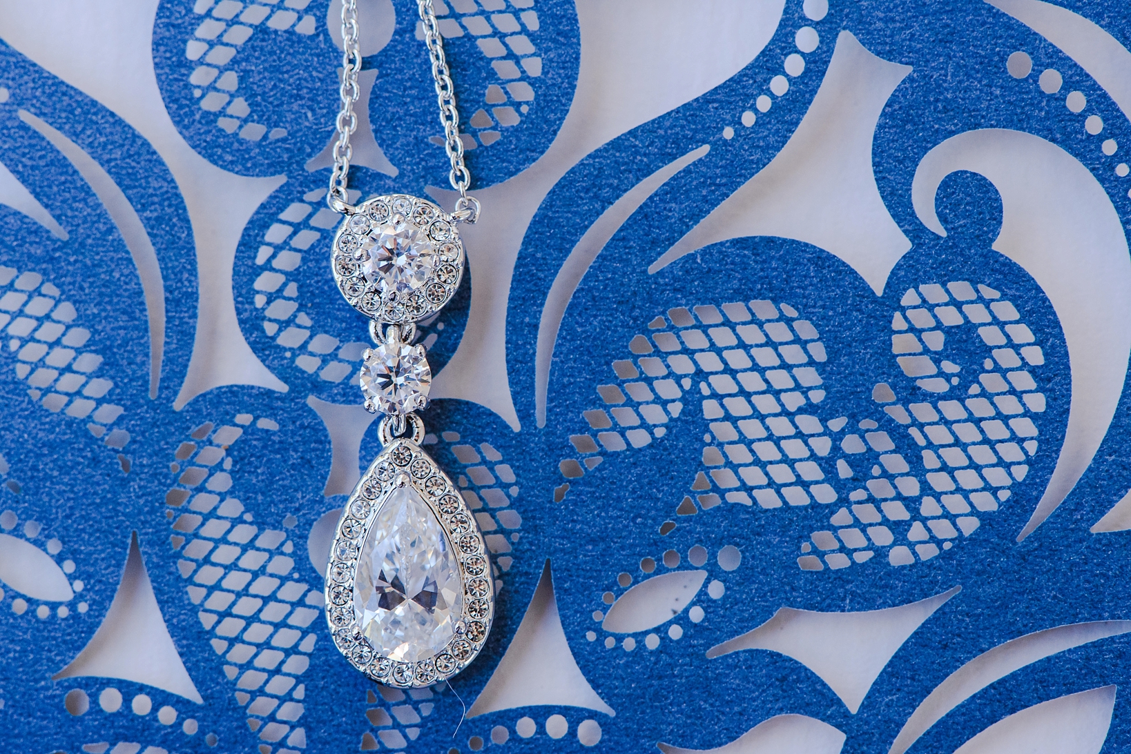 Bride's necklace against a lace-cut wedding invitation