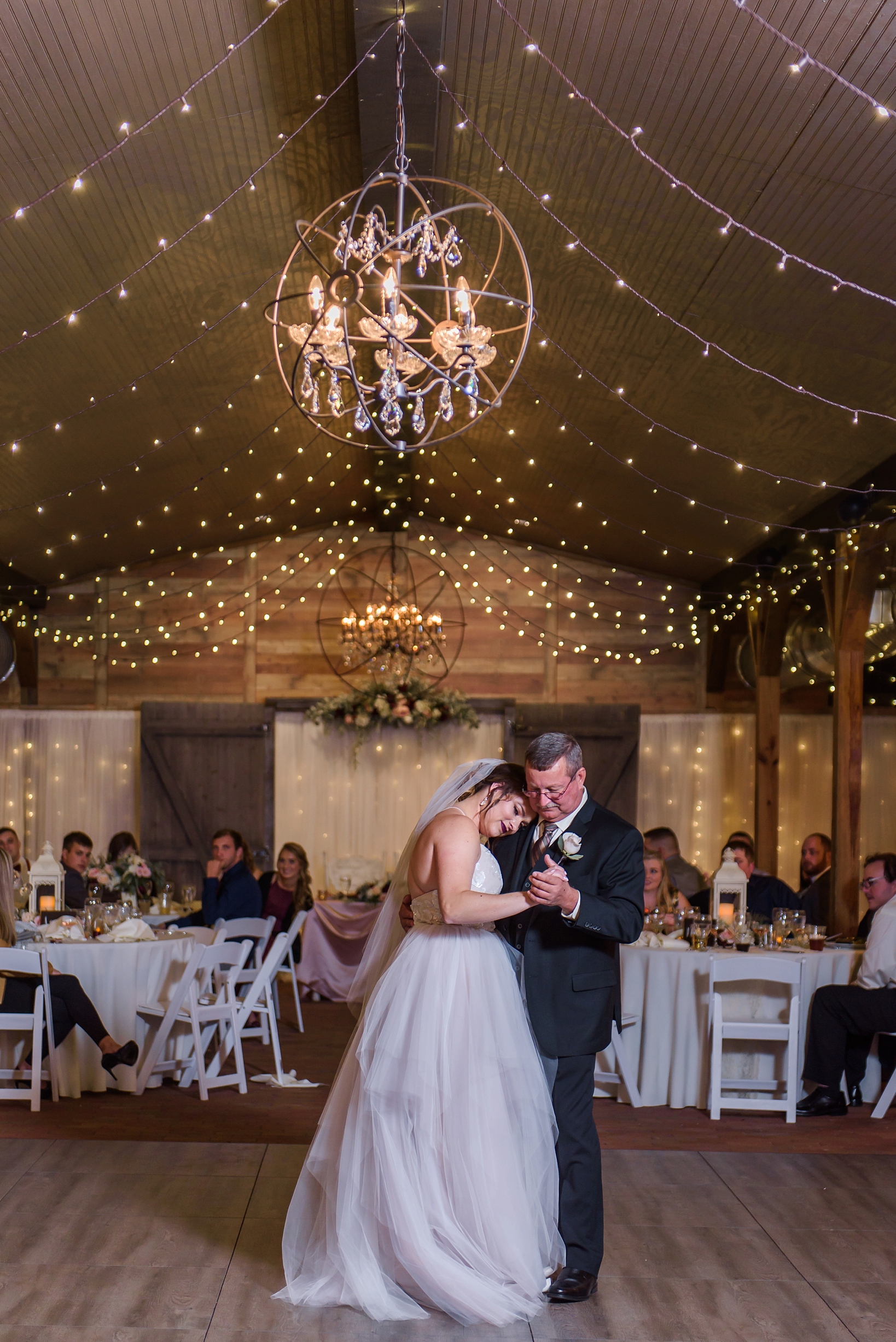 Father daughter dance in a rustic barn covered in string lights