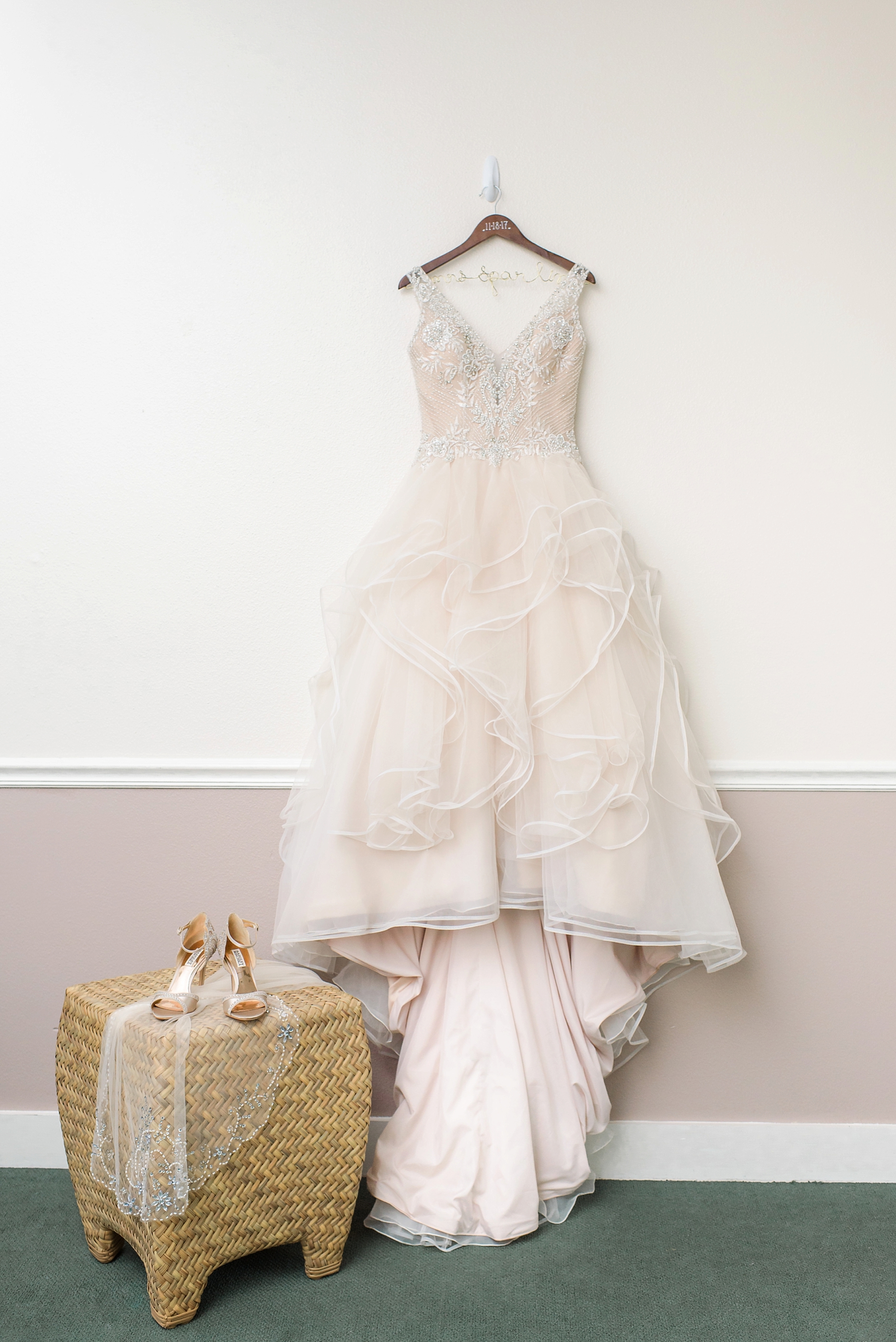 The wedding dress hanging next to the shoes and veil on a customized wooden hanger