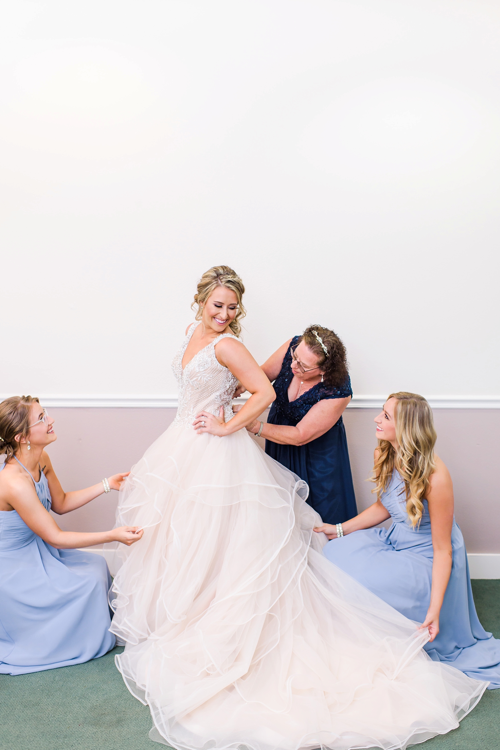 The mother of the bride and bridesmaids helping the bride into her dress by Sarah & Ben Photography