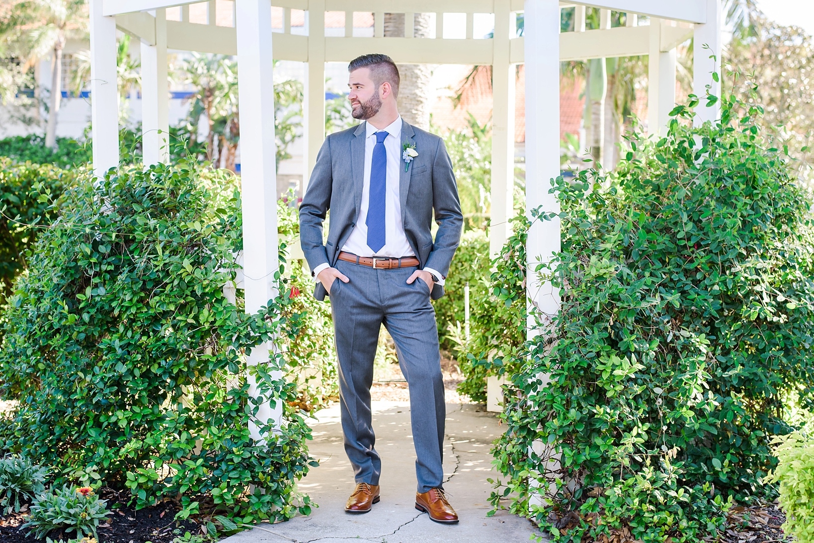 Groom in a perfectly fitted suit standing between two hedges
