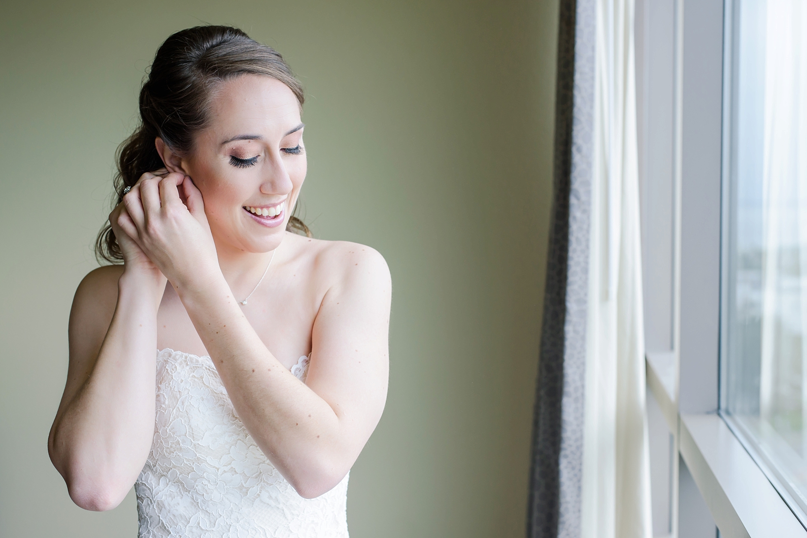Bride putting her jewelry on in front of a window