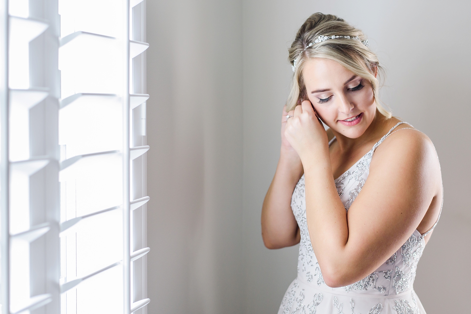 Bride putting her earrings in surrounded by natural sunlight in her Hayley Paige dress