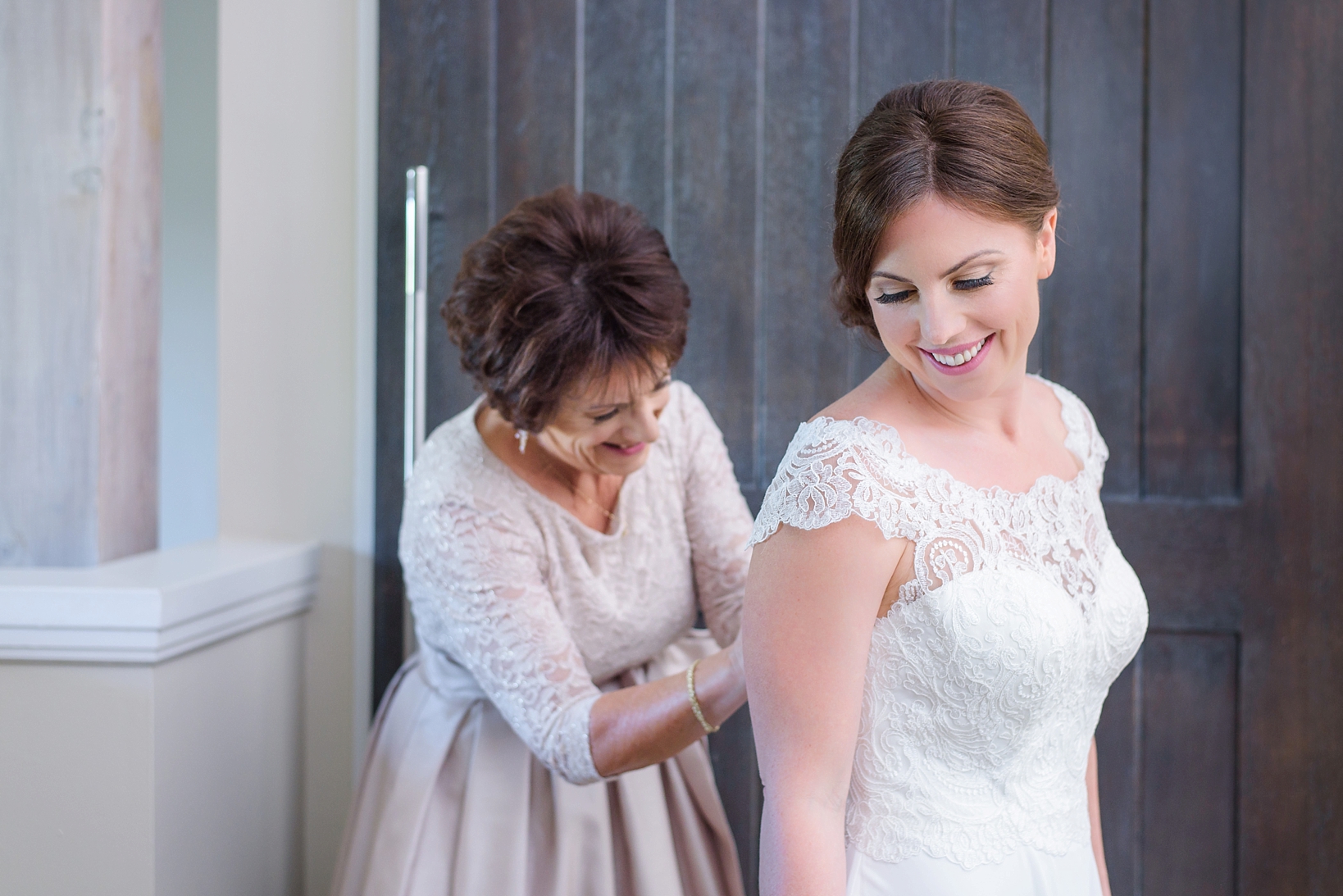 Mother of the Bride helping her daughter into her lacy wedding dress