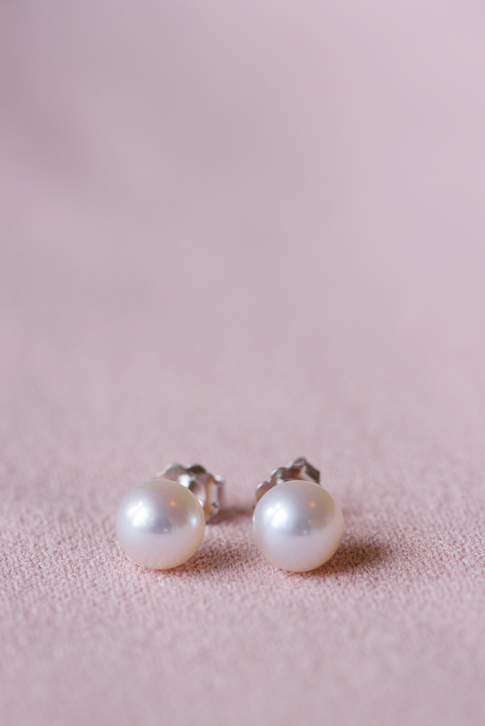 Pearl earrings against a blush background