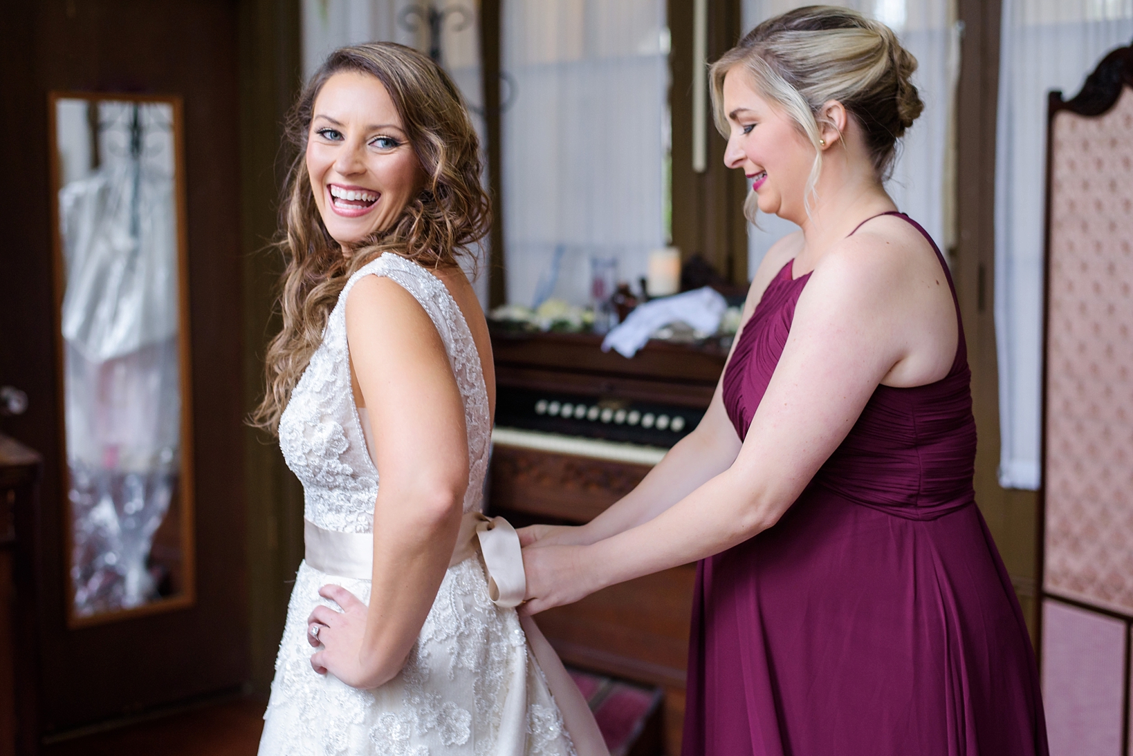 Bride laughs as her bridesmaid helps with some finishing touches of tying a bow