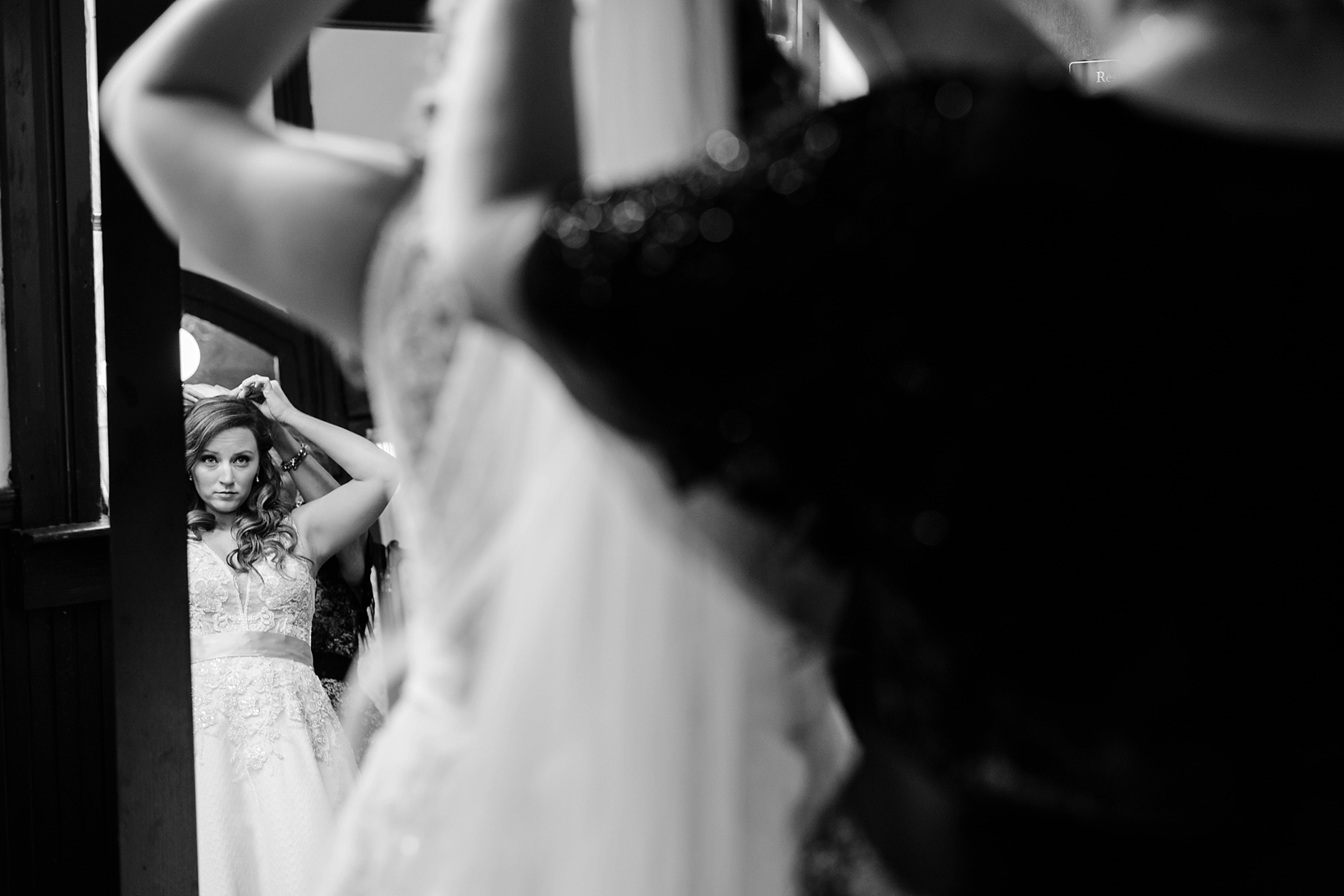 Black and White image of the Bride looking in a mirror for one last check up before walking down the aisle