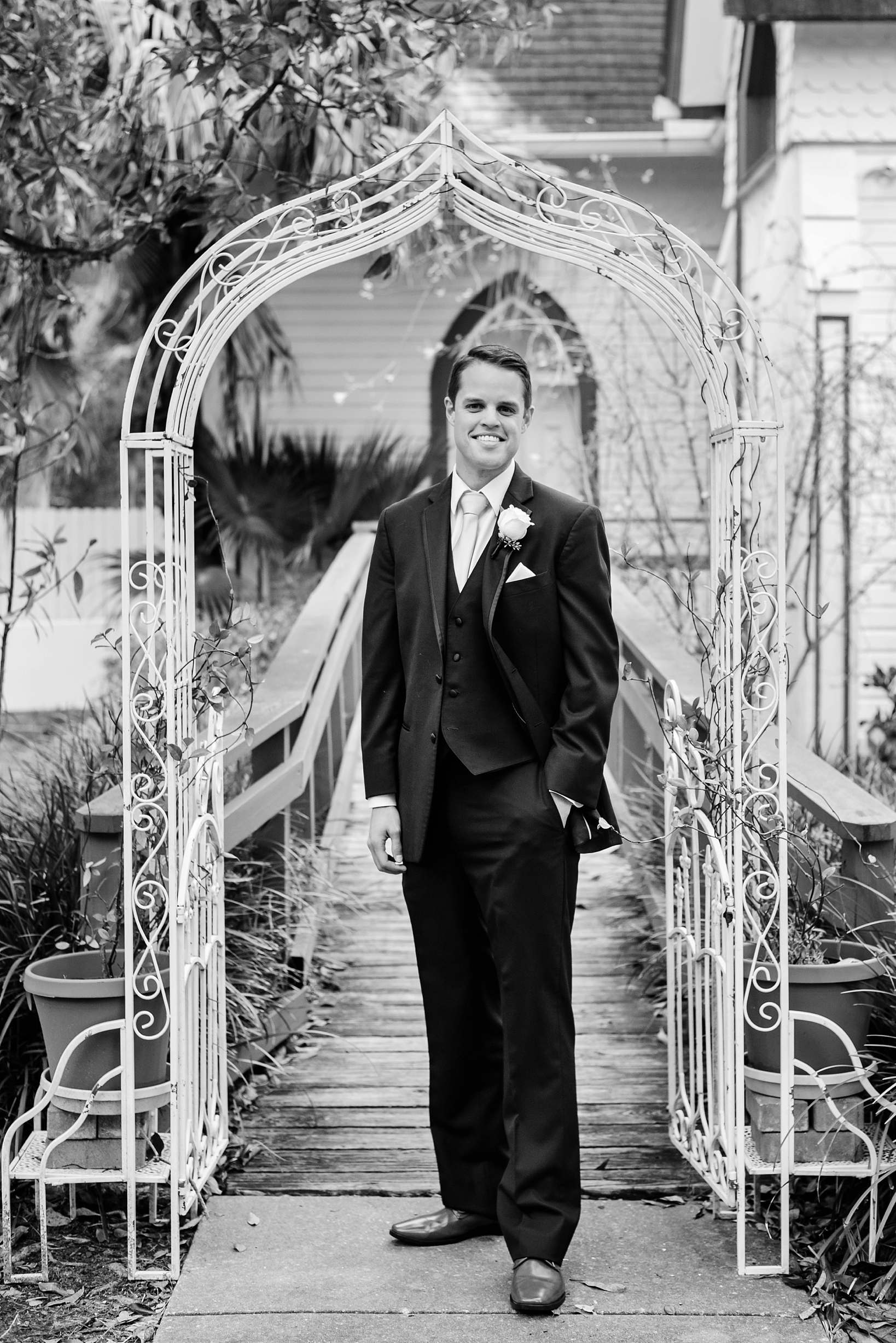 Black and White image of a Groom standing under a metal trellis in Dunedin, FL by Sarah & Ben Photography. Check out all our work at www.sarahben.com