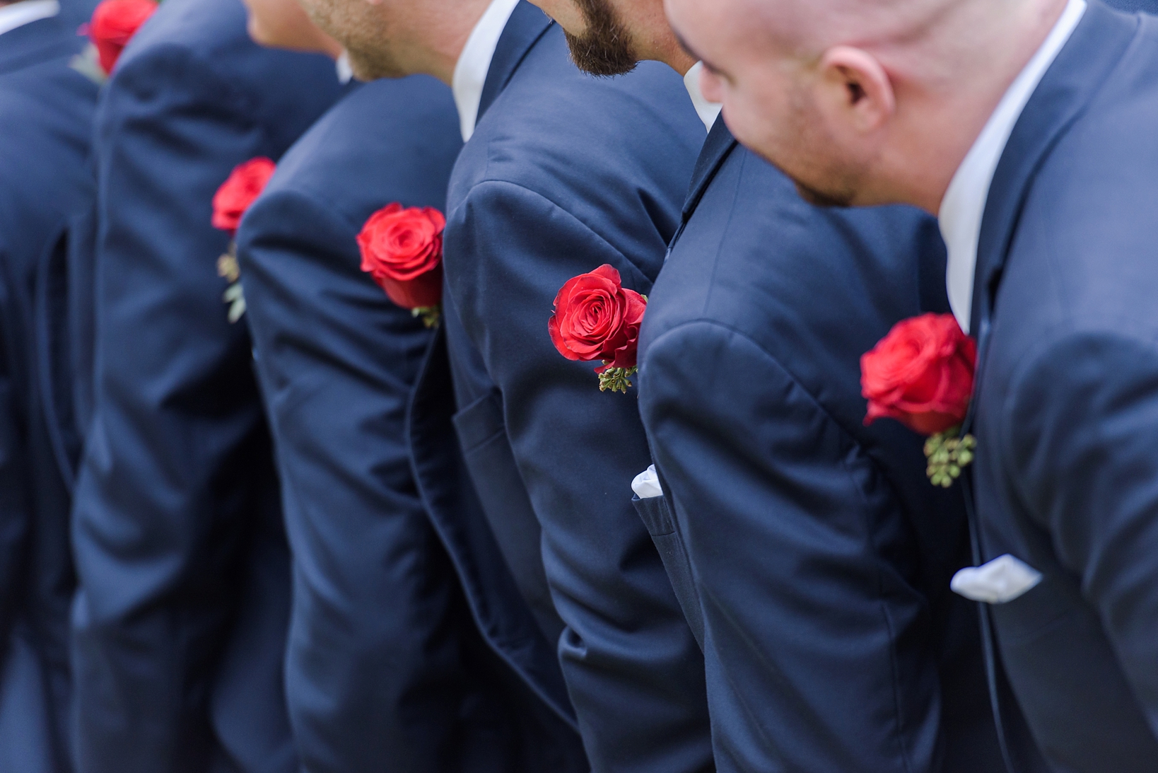 A row of red roses along the groomsmen's lapels by Sarah & Ben Photography. Check out all our work at www.sarahben.com