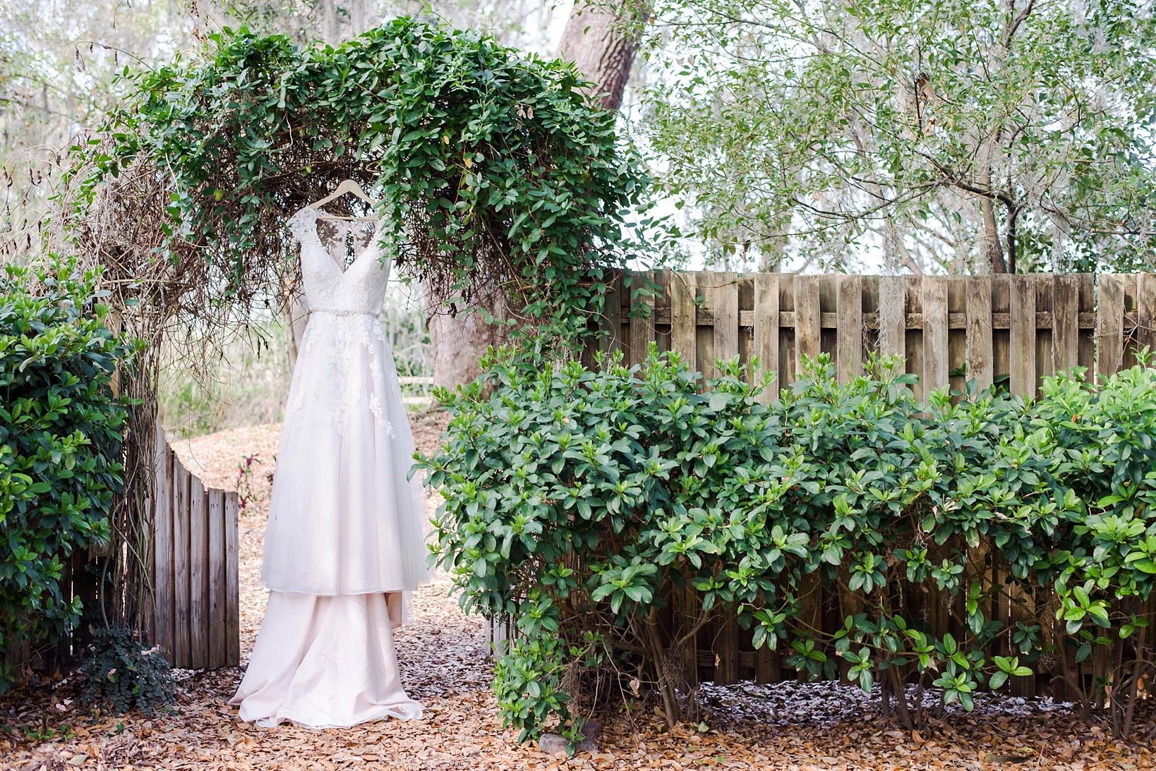 The wedding dress hanging in a rustic greenery filled arch