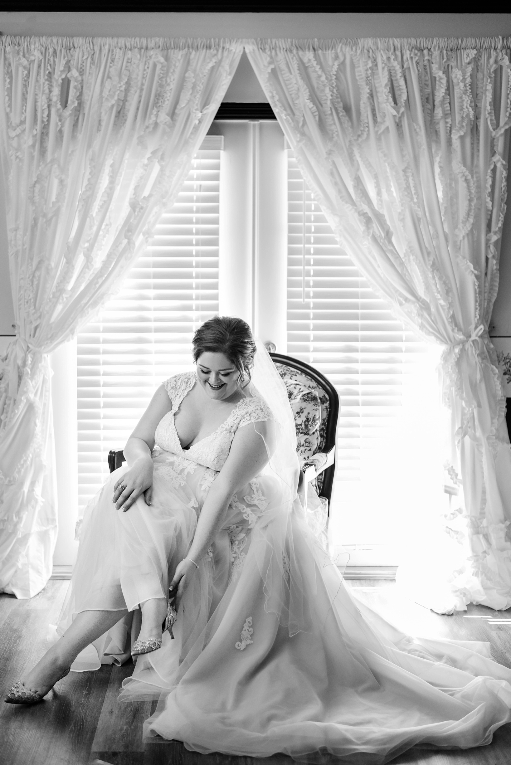 Bride putting her wedding heels on silhouetted by the sunlight from the window