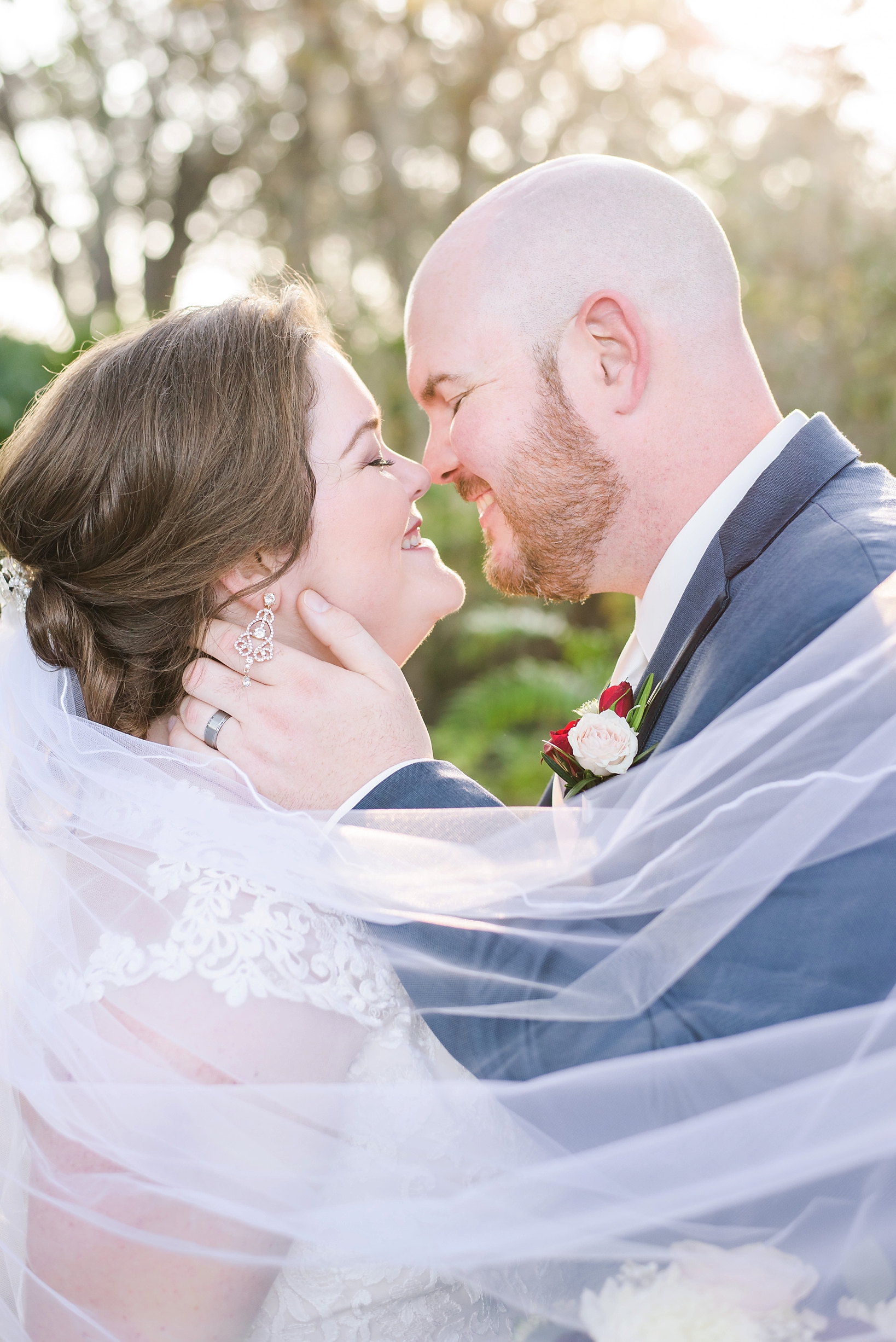 Bride and groom wrapped in her veil, made transparent by the sun light by Sarah & Ben Photography