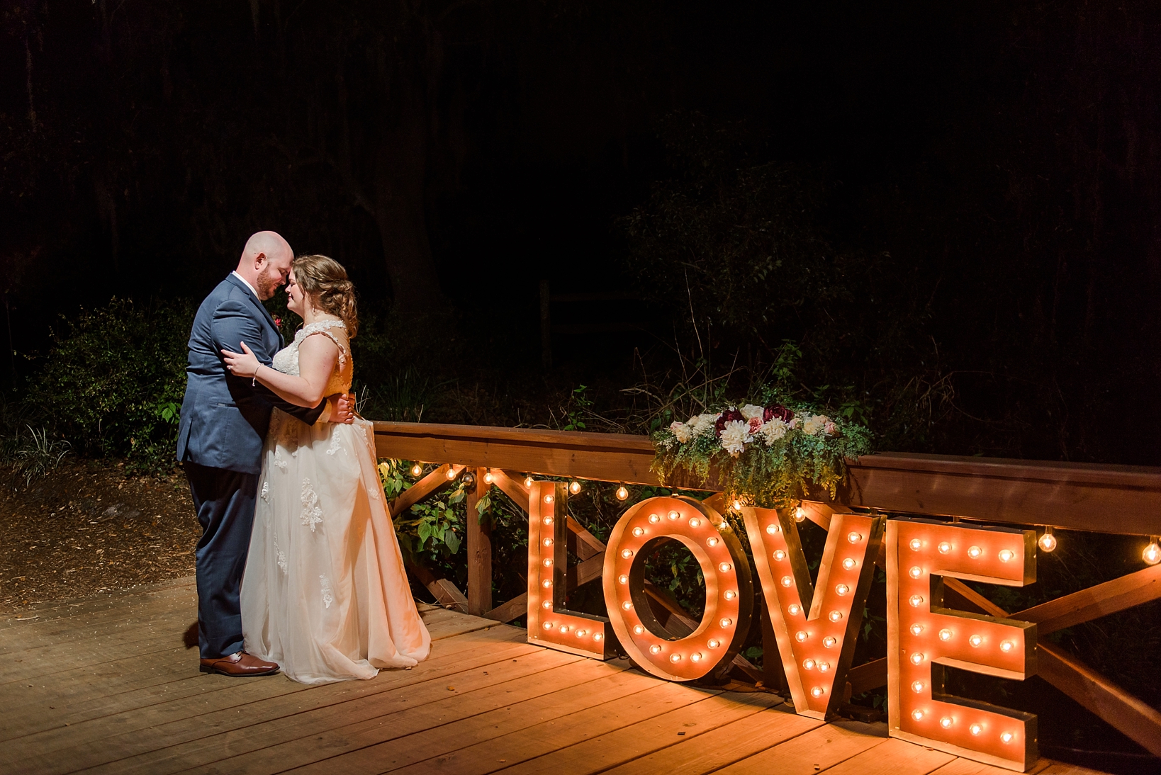 Bride and groom with "Love" sign glowing in the night