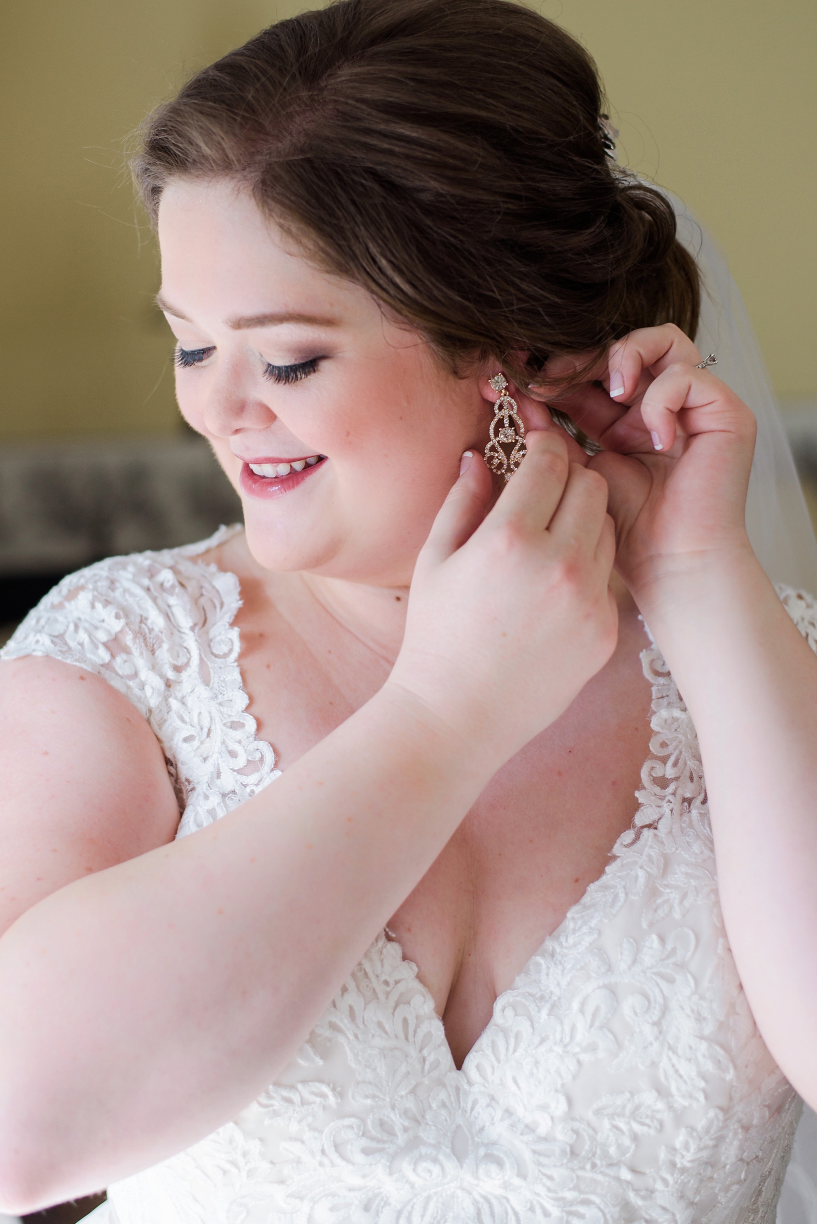 The bride in her lace trimmed wedding dress putting her earrings in