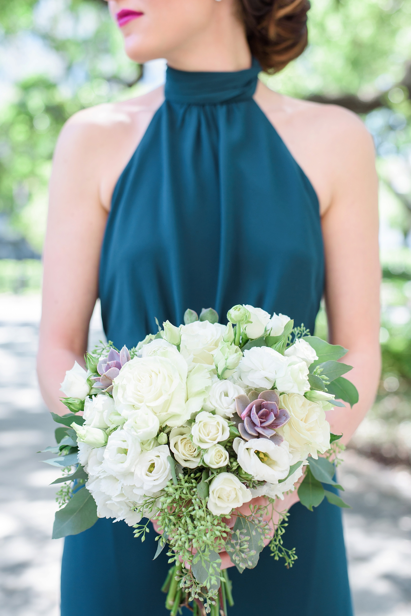 Bridesmaid in teal dress holding her floral filled bouquet