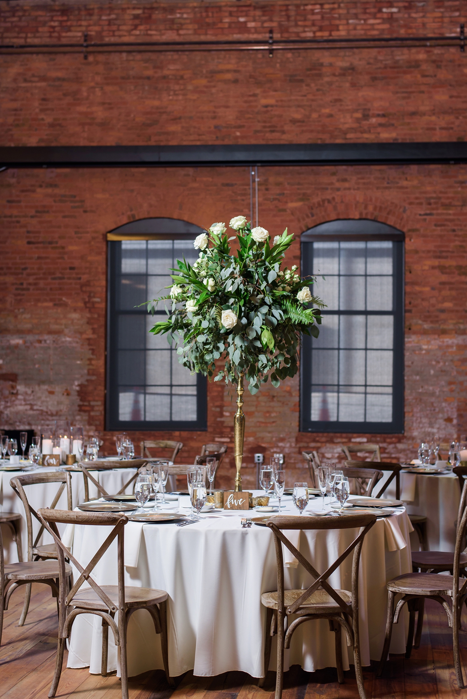 Wedding reception table with large floral centerpieces and rustic wooden chairs