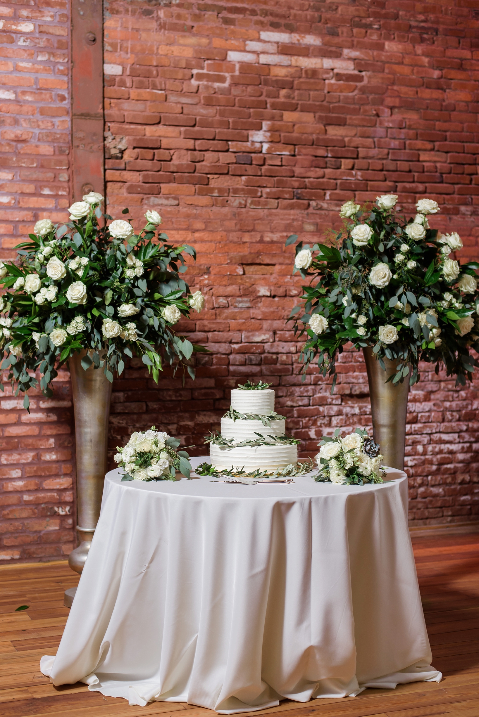 The wedding cake with eucalyptus leaves accenting the table with brick wall background